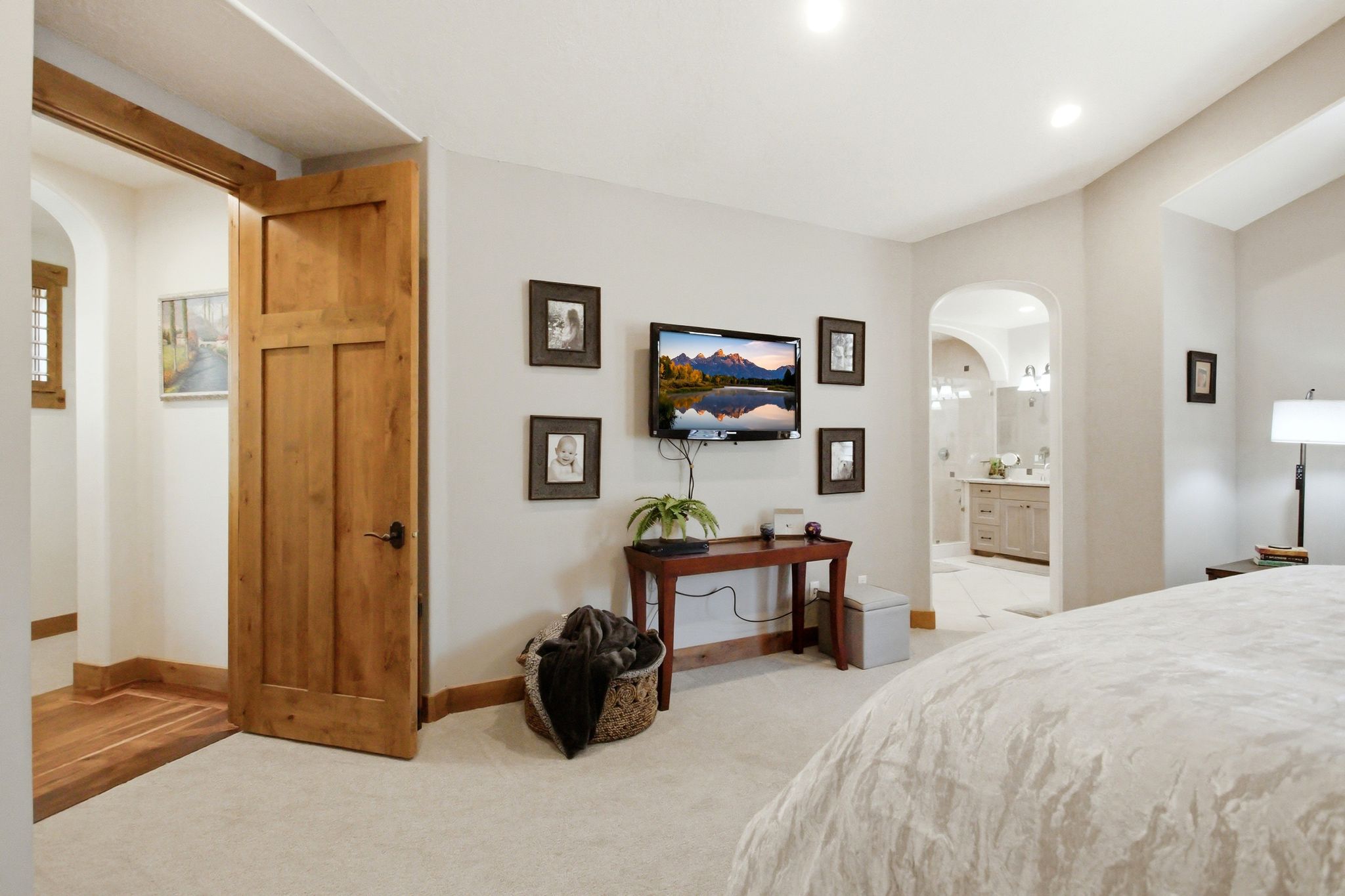 Carpeted sleeping area featuring a wood-panel door, recessed lighting, and an arched entry to a bathroom with a double vanity and sconce lighting