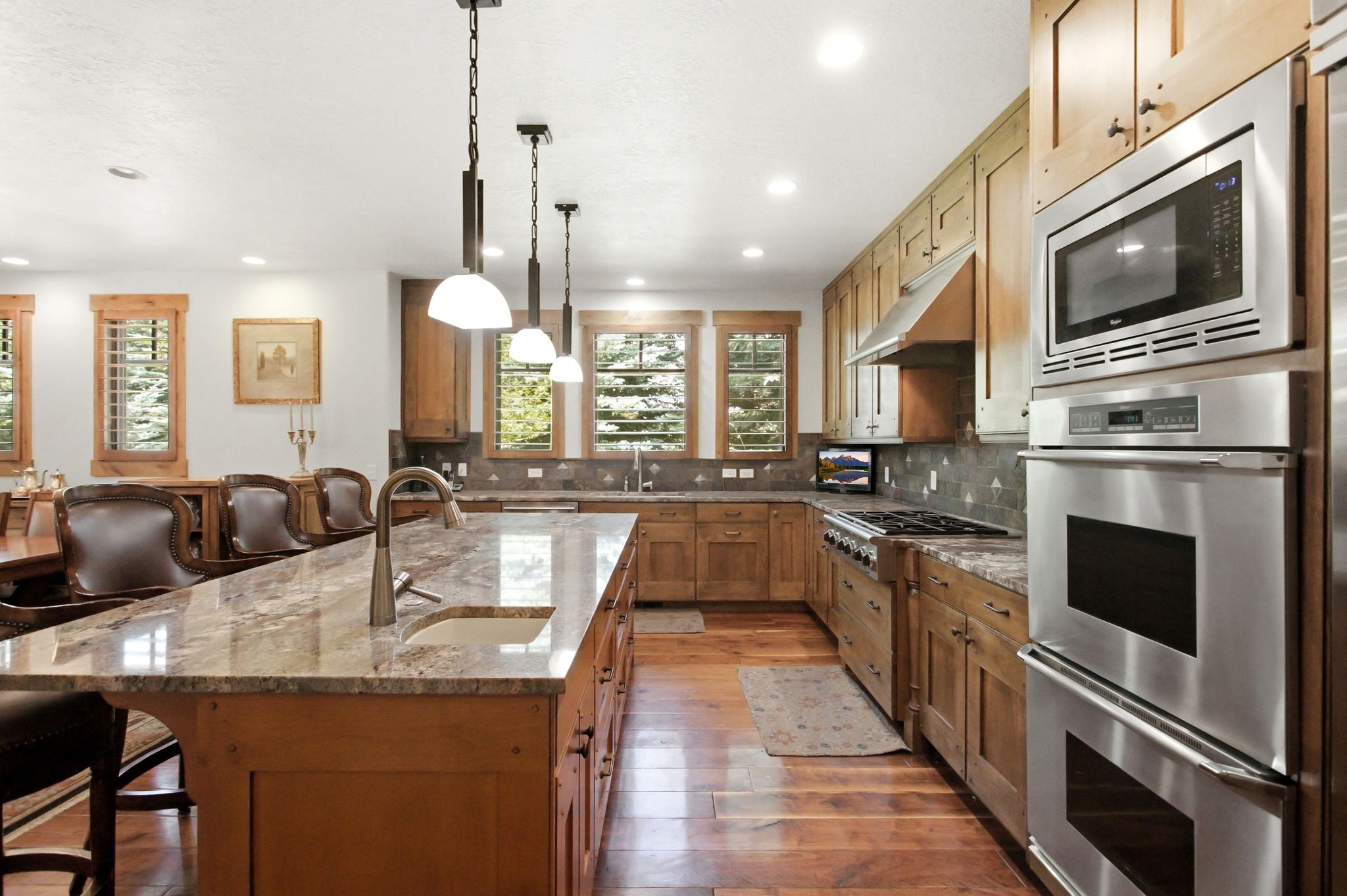Kitchen featuring a large central island with a built-in sink, granite countertops, wood-finish flooring, stainless steel appliances, and wood cabinetry