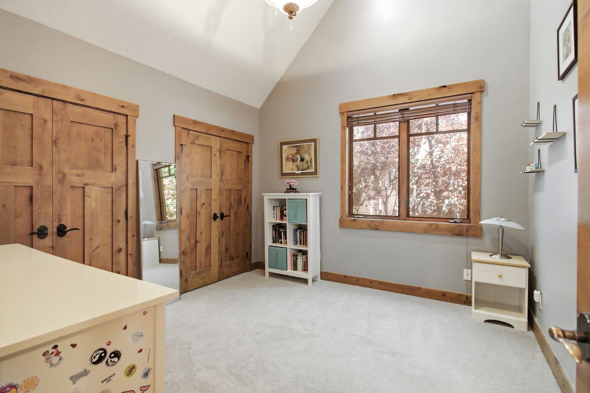 Vaulted ceiling room featuring natural wood trim, a large window, light gray walls, and light-colored carpeting