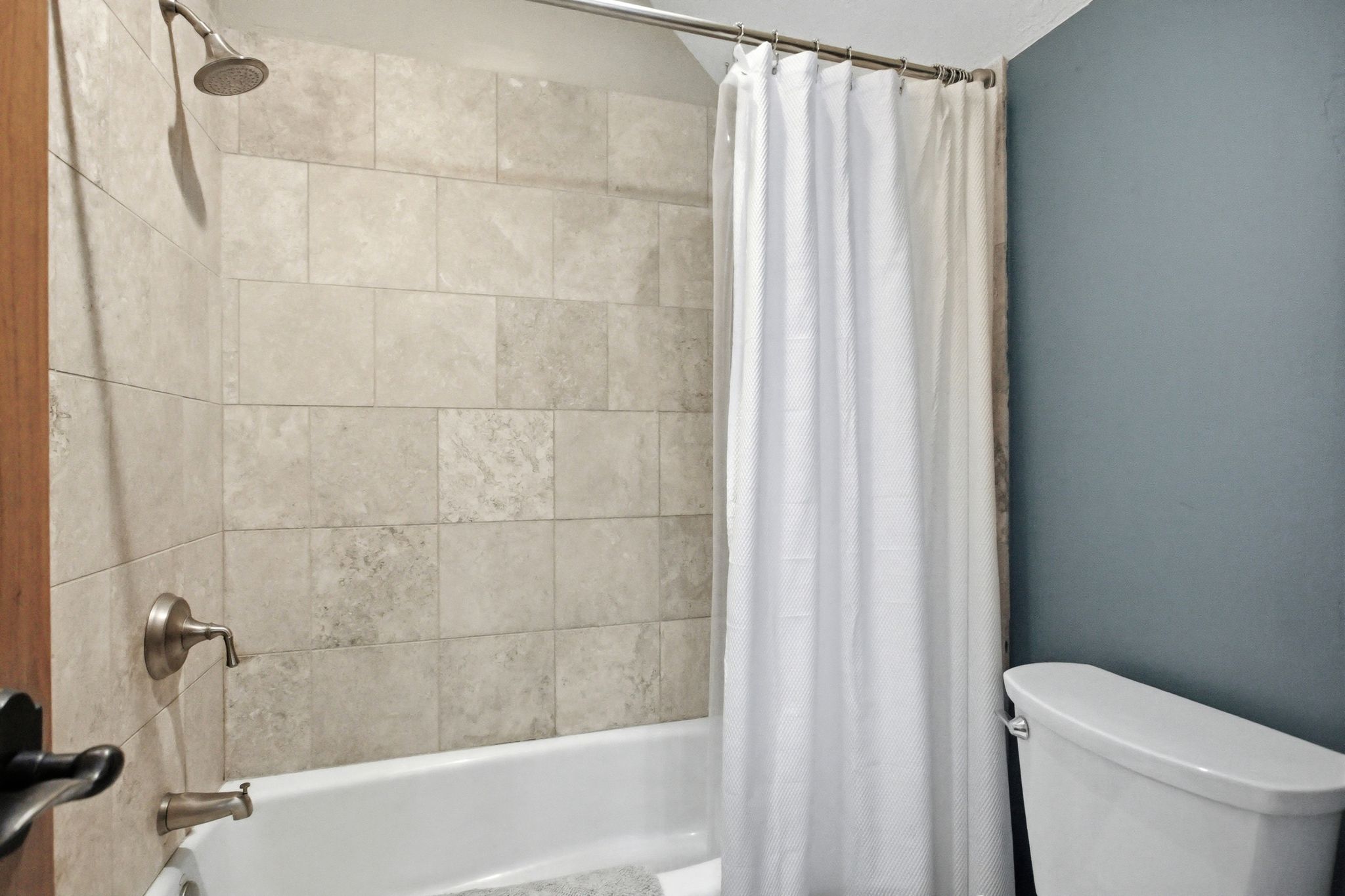 Bathtub-shower combination featuring neutral-toned subway tile surround, brushed nickel fixtures, and a white porcelain tub