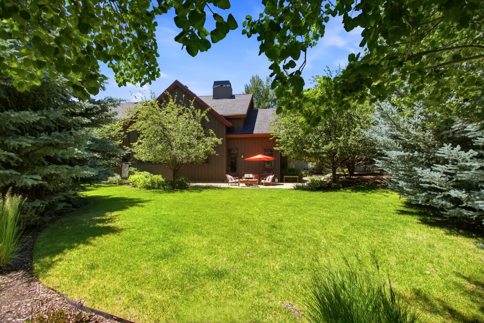 Spacious rear yard with expansive lawn, mature tree landscaping, and a patio area