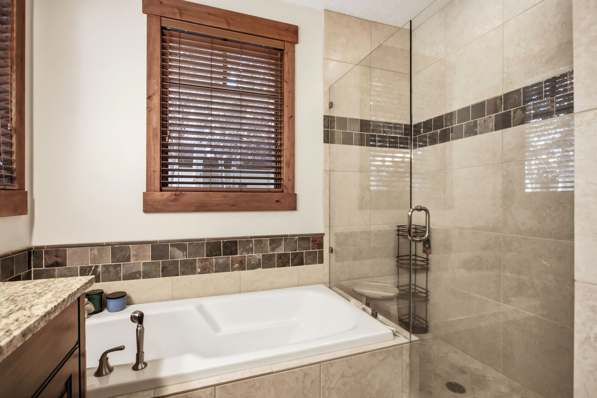 Bathroom featuring a built-in tub with brushed nickel fixtures, a glass-enclosed shower, wood-framed windows with blinds, and tile wainscoting