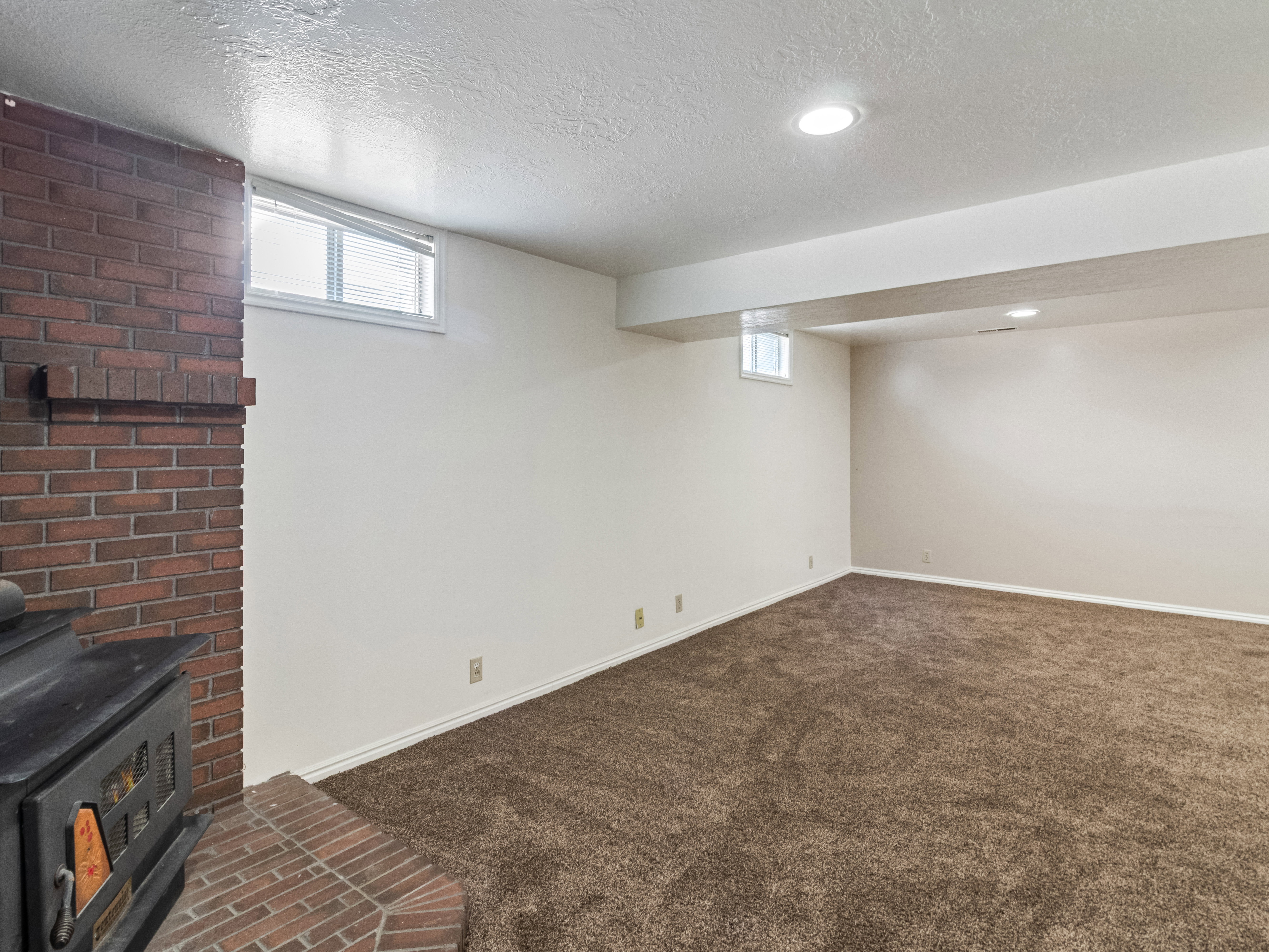 Spacious room featuring brick fireplace with hearth, recessed lighting, and rich brown carpeting