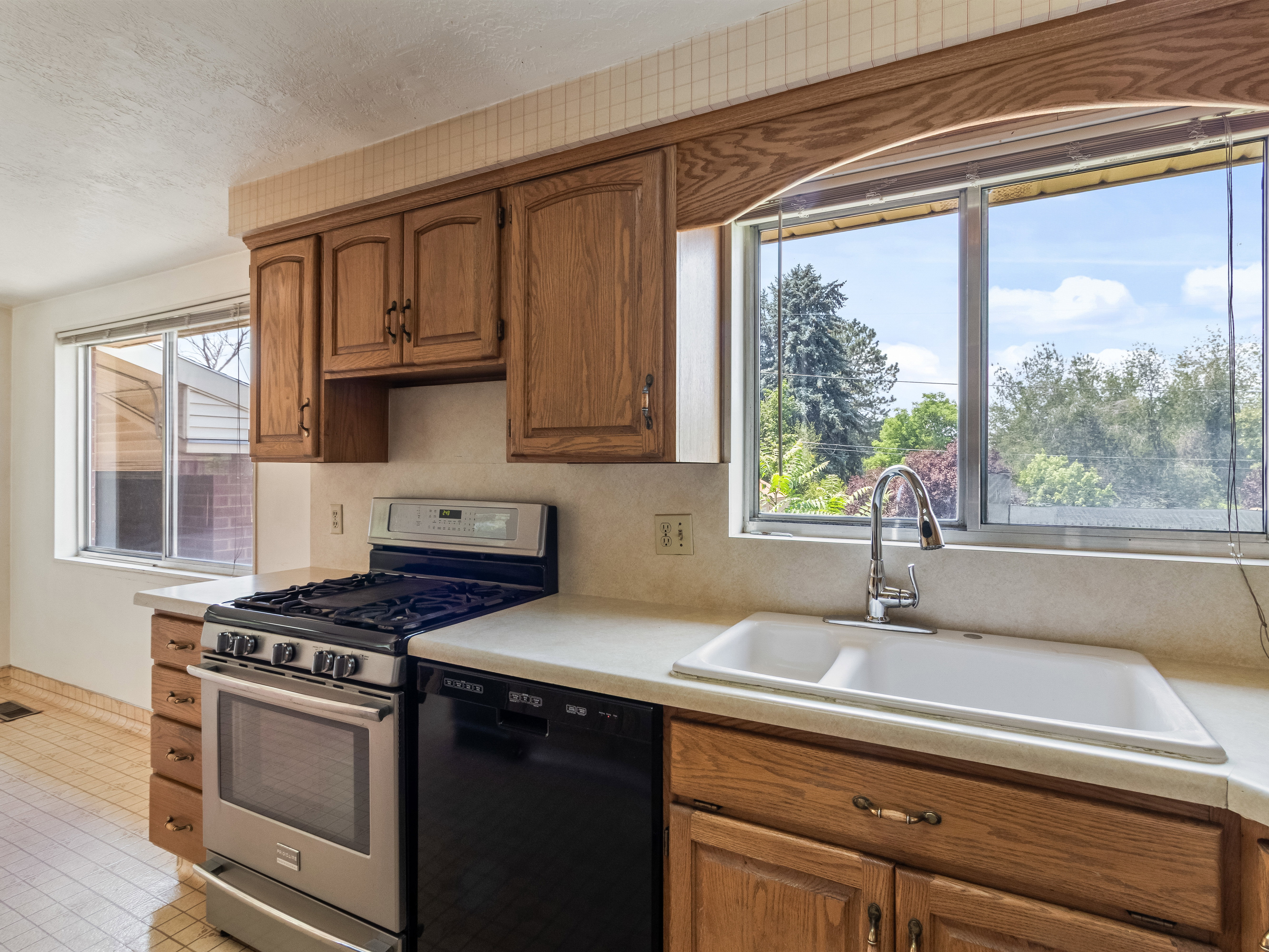 Kitchen featuring natural wood cabinetry, light-toned countertops, a stainless steel gas range, and a double basin sink with a high-arch faucet