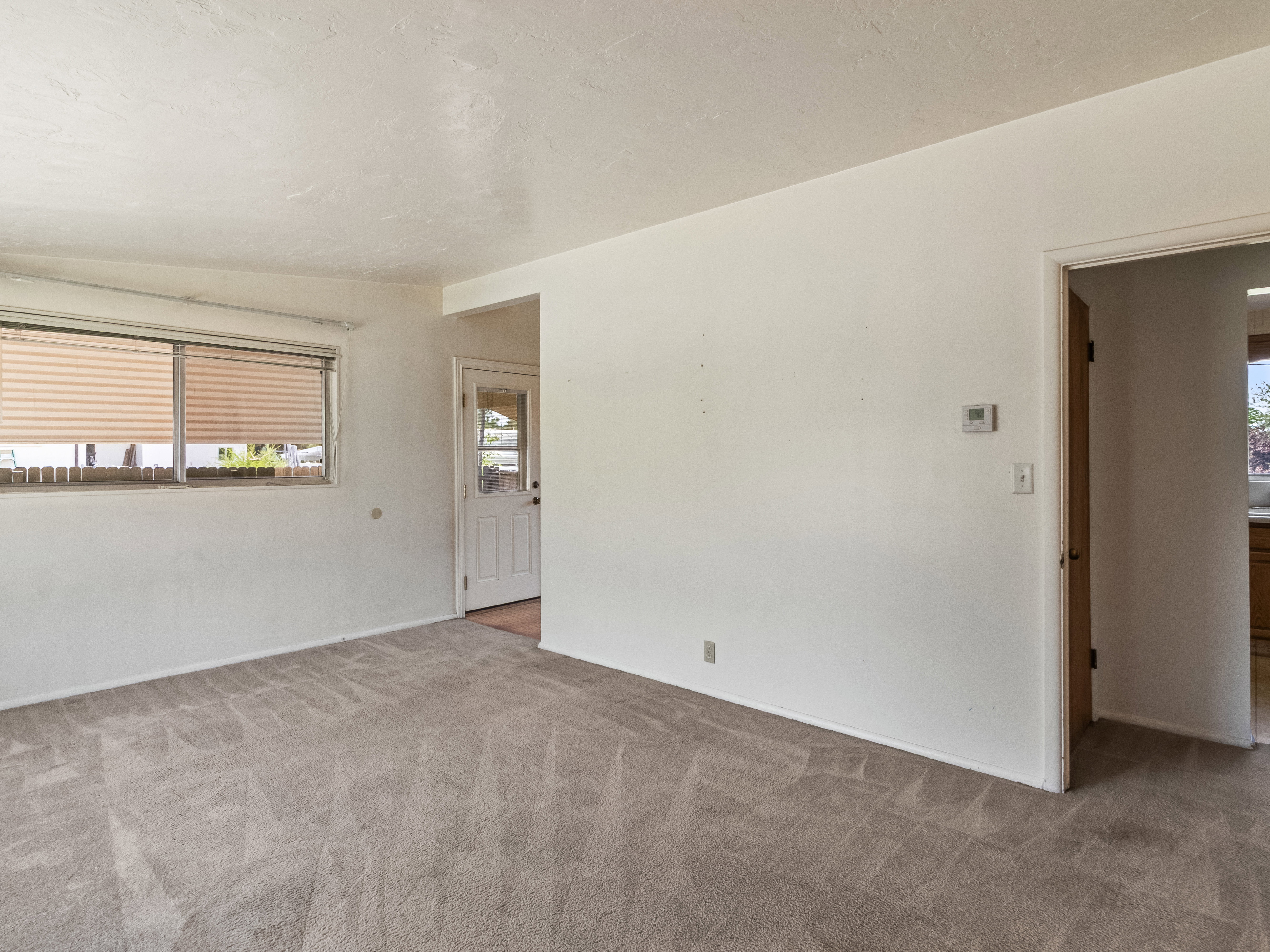 Living area featuring light-colored carpet, white walls, and a window with horizontal blinds