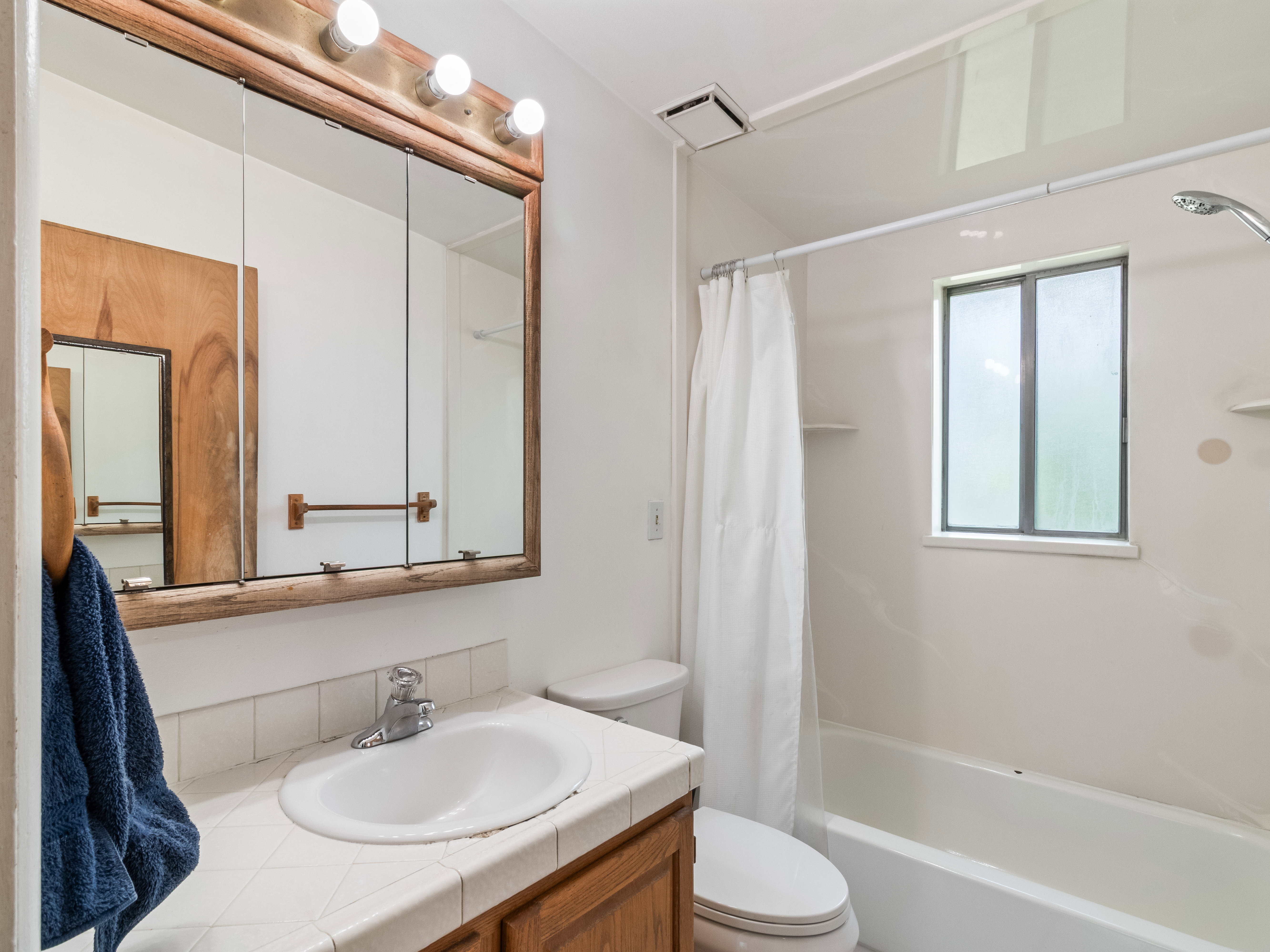 Full bathroom featuring a single vanity with a tile countertop, a framed medicine cabinet with integrated lighting, a tub/shower combination, and a window for natural light