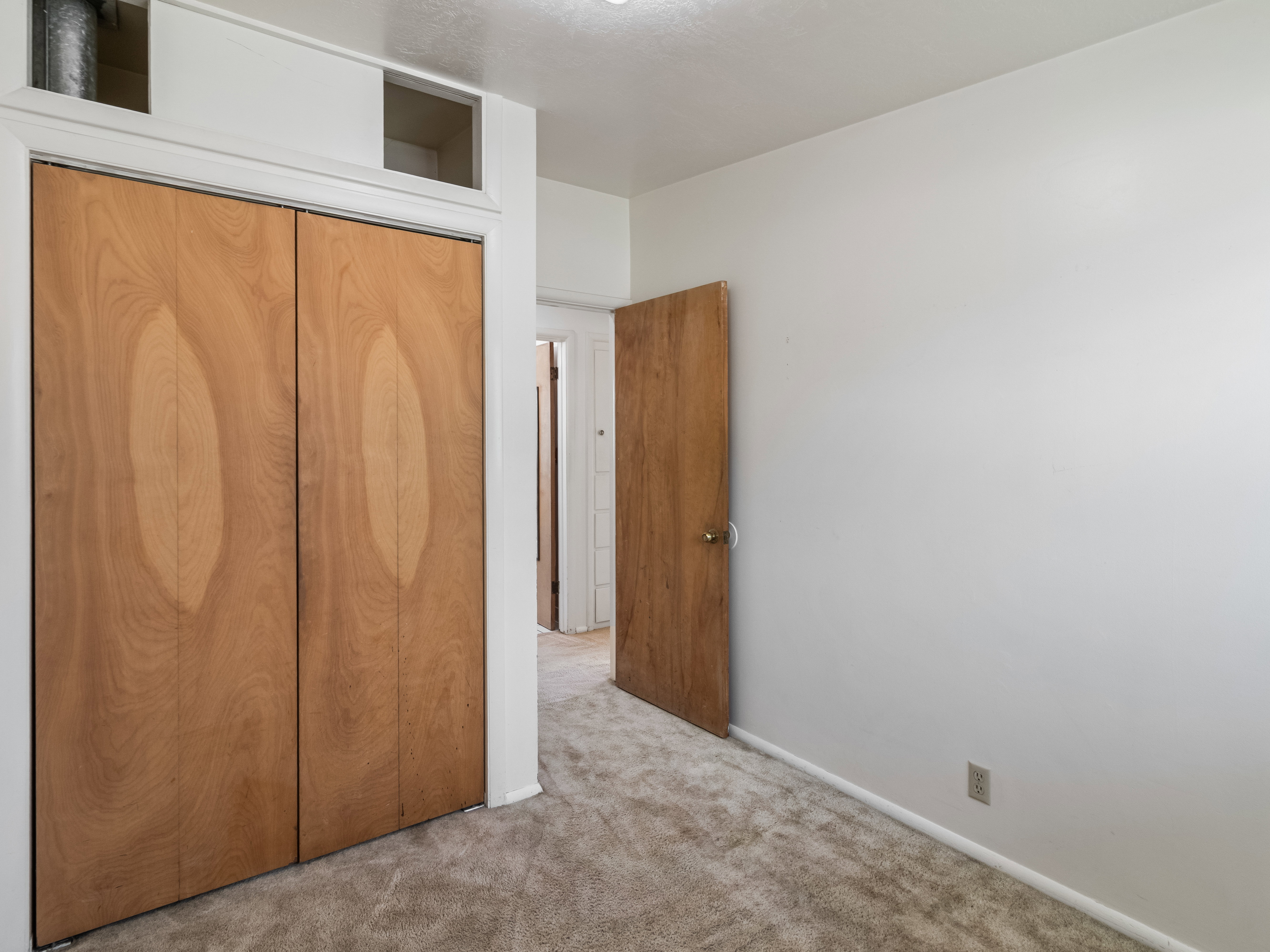 Carpeted room featuring wood-finish bi-fold closet doors, white trim, and a light-colored wall finish