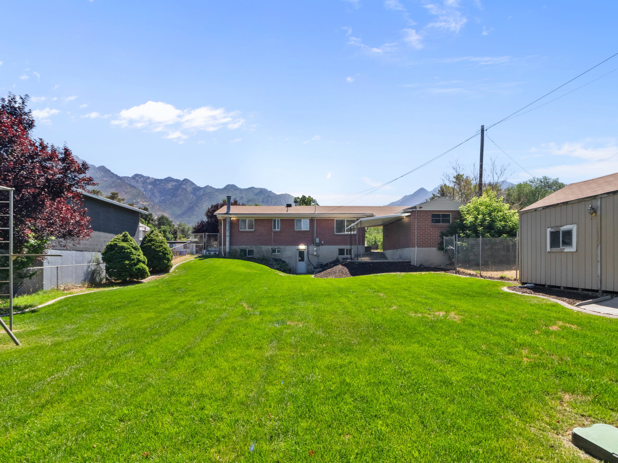 Expansive rear lawn featuring a detached shed, chain-link fencing, and a mountain backdrop