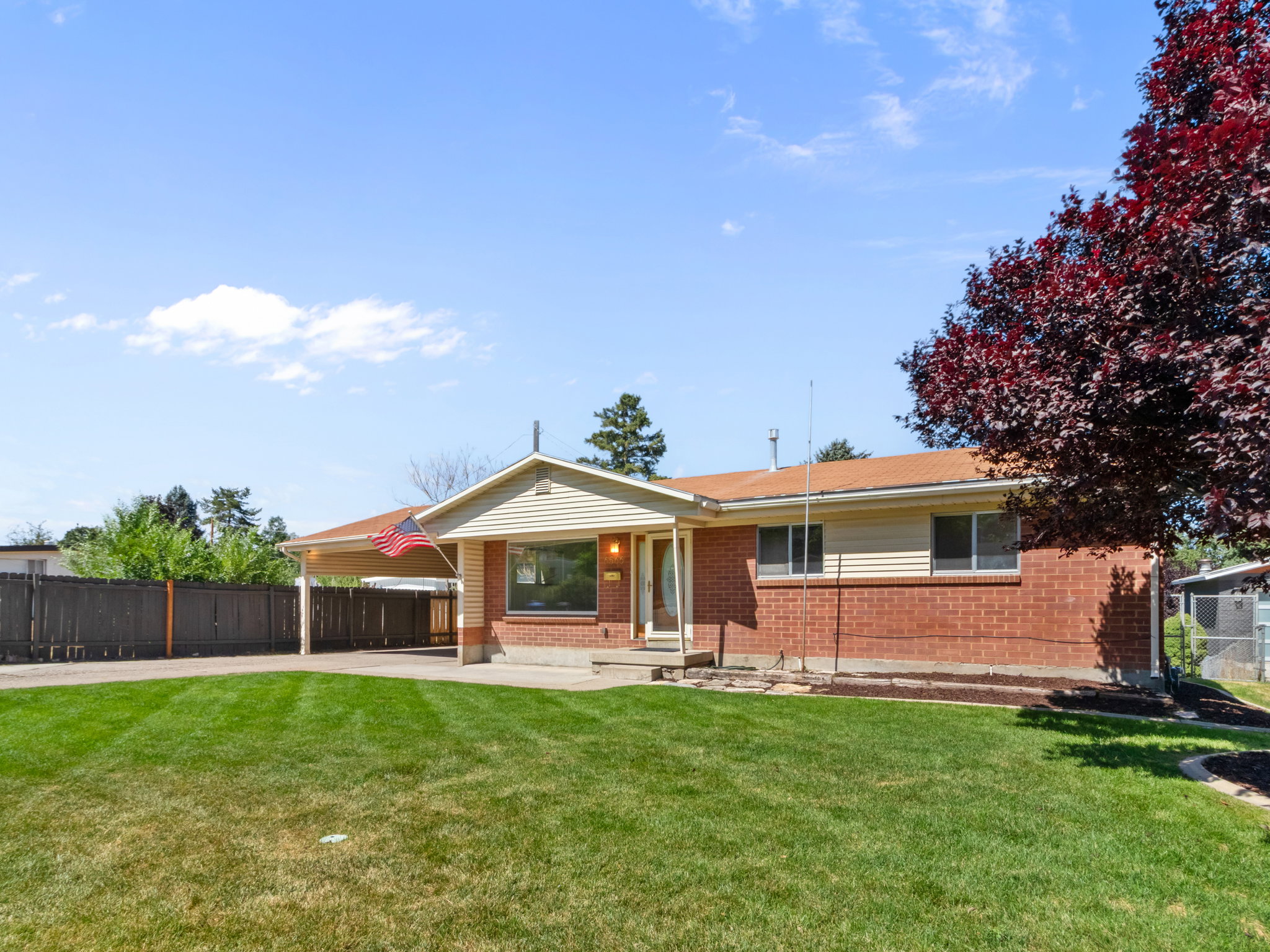Brick exterior featuring an attached carport, front lawn, and mature landscaping