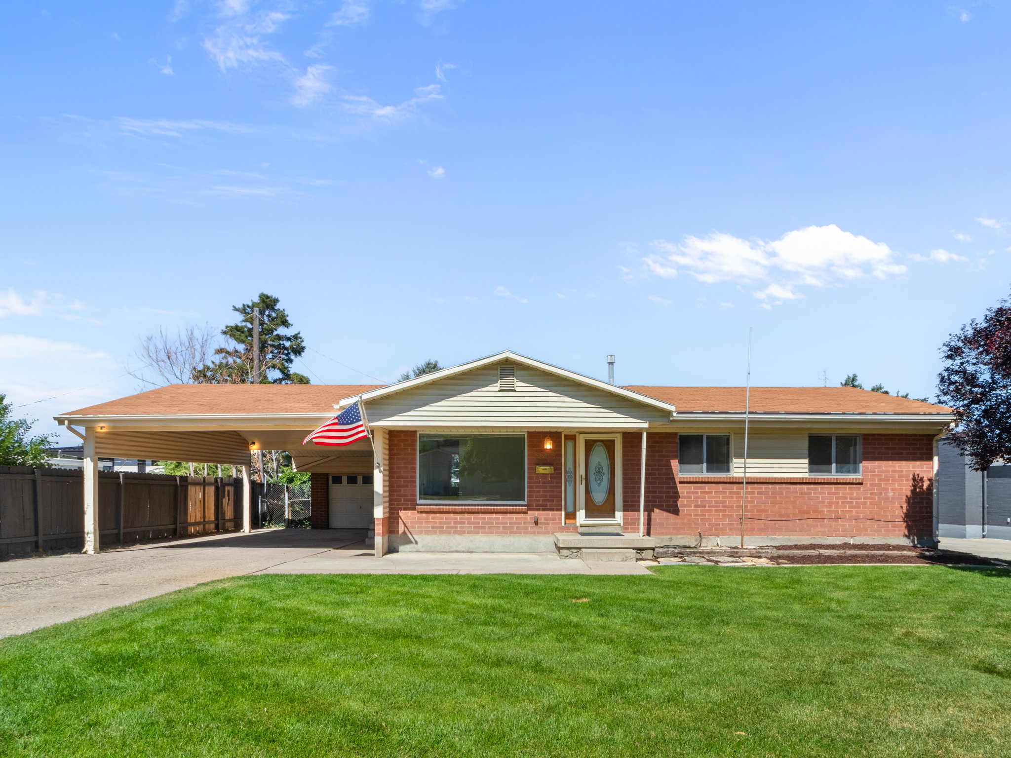 Brick exterior home featuring a covered carport, attached garage, and a manicured lawn