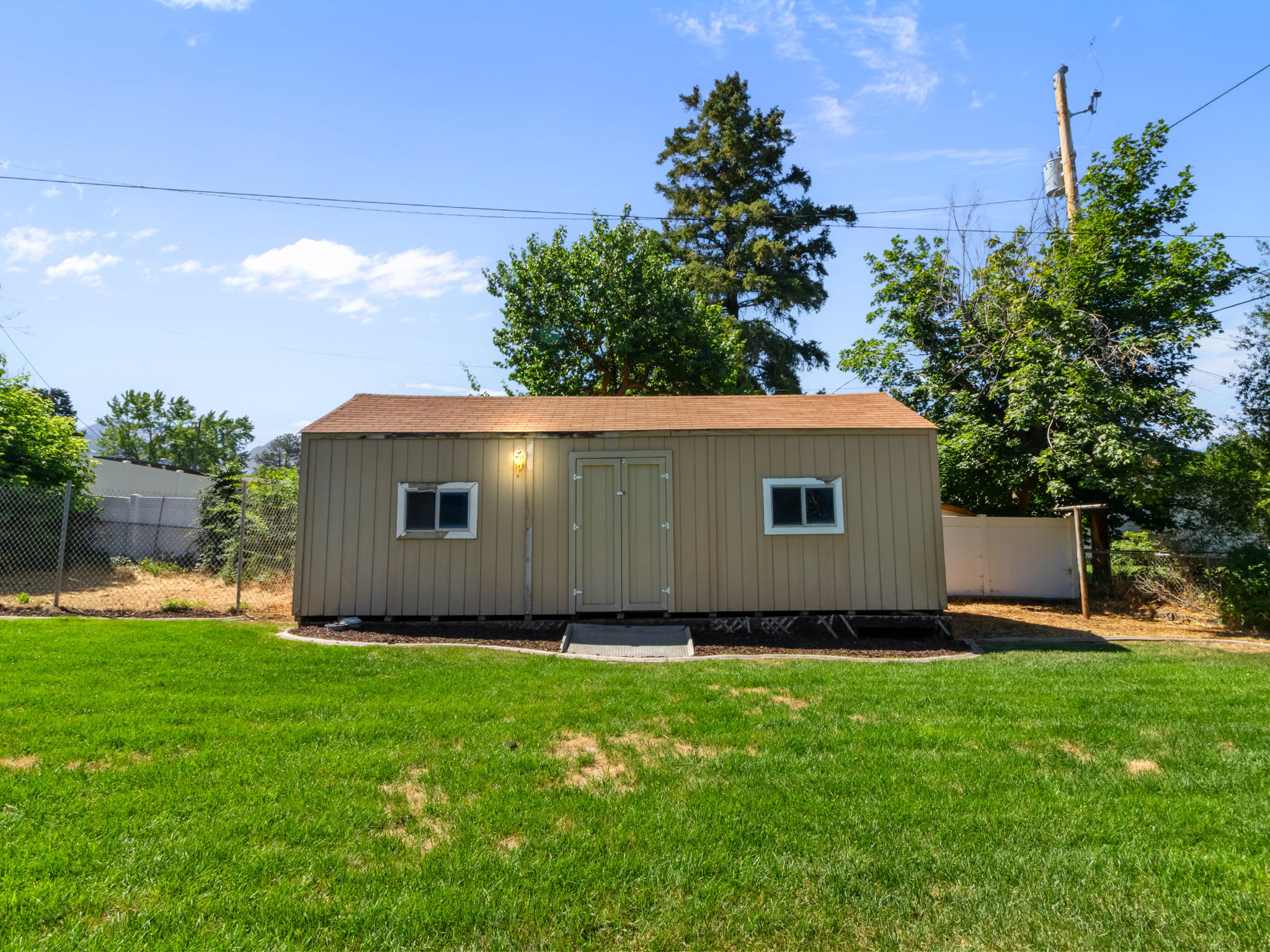 Detached shed with light tan siding, a brown shingled roof, and dual windows