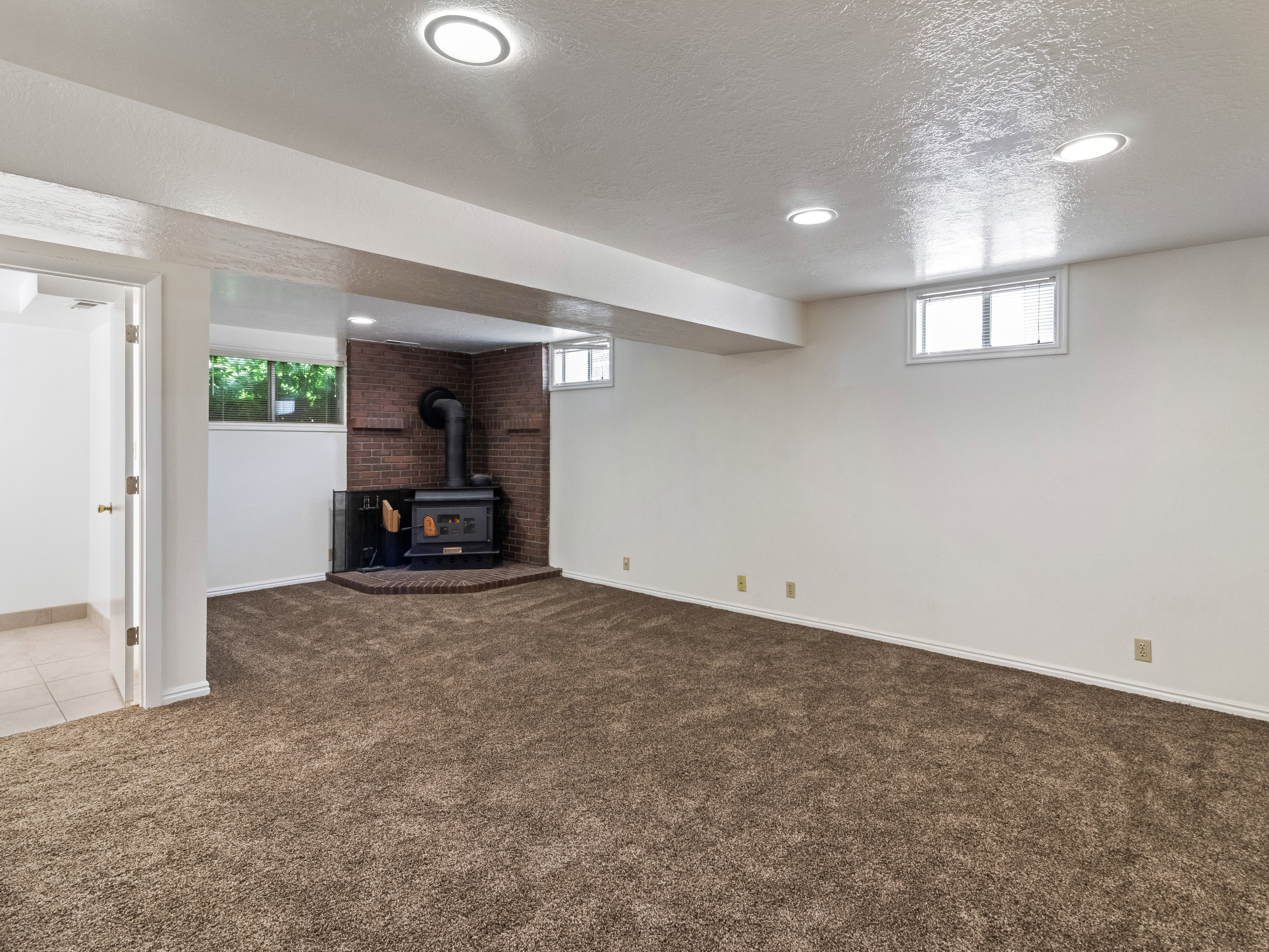 Spacious room featuring a corner wood-burning stove with a brick surround, recessed lighting, and carpeted flooring