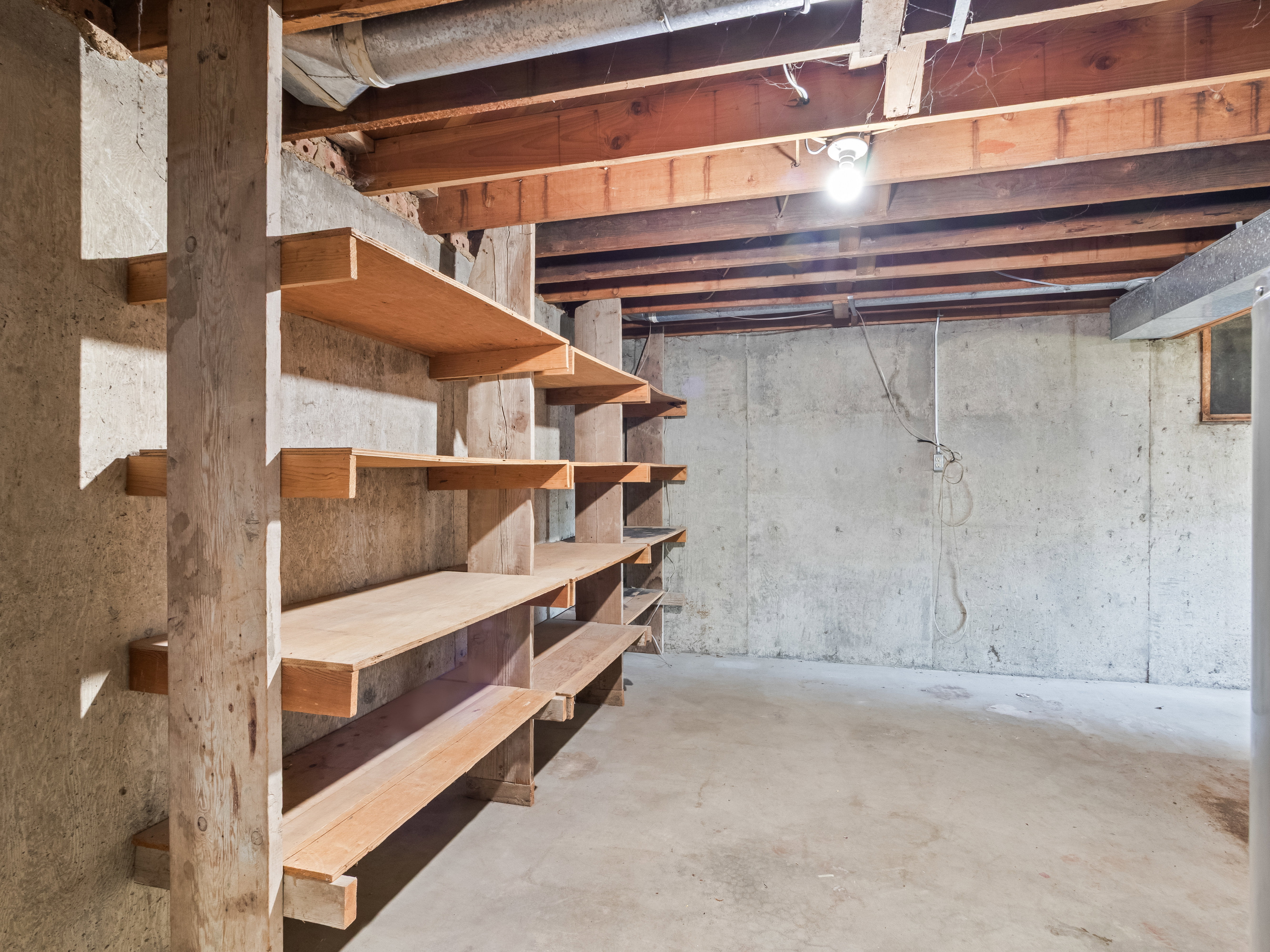 Concrete foundation walls featuring built-in wooden shelving, exposed wooden ceiling joists, and a concrete floor