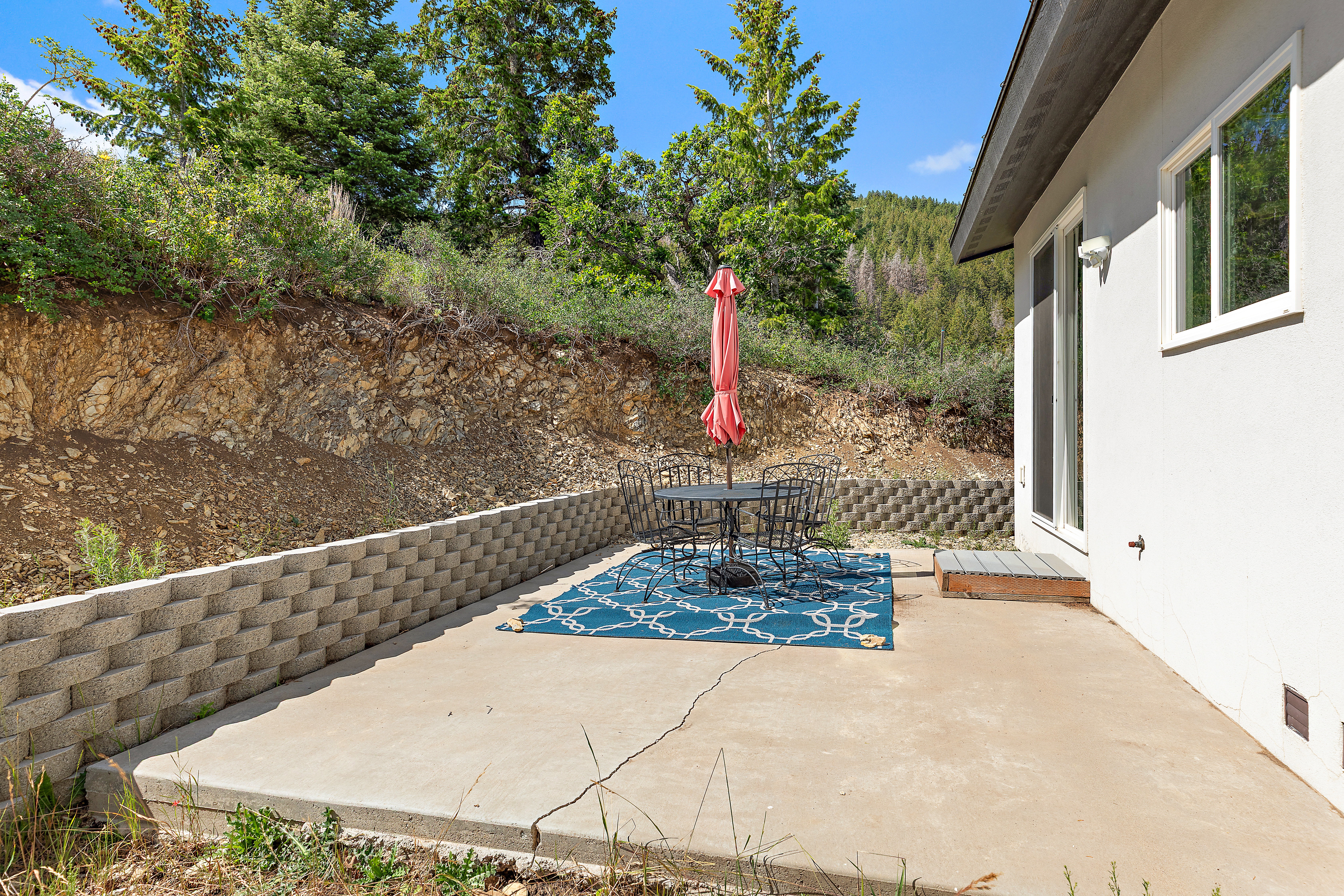 Poured concrete patio featuring a block retaining wall, stucco exterior, and a sliding glass door