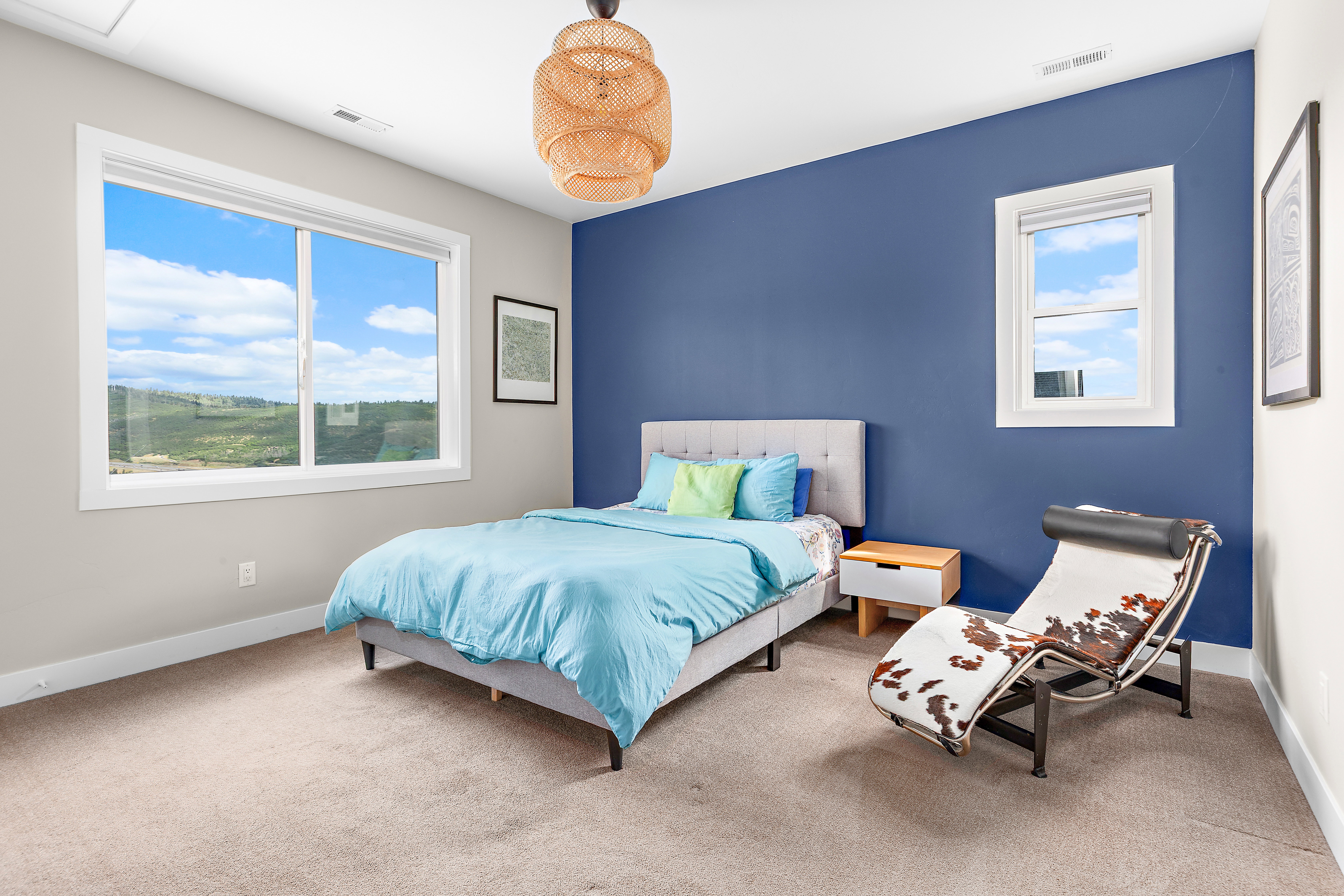 Carpeted room featuring a large sliding window, an additional window, a blue accent wall, and a woven pendant light fixture
