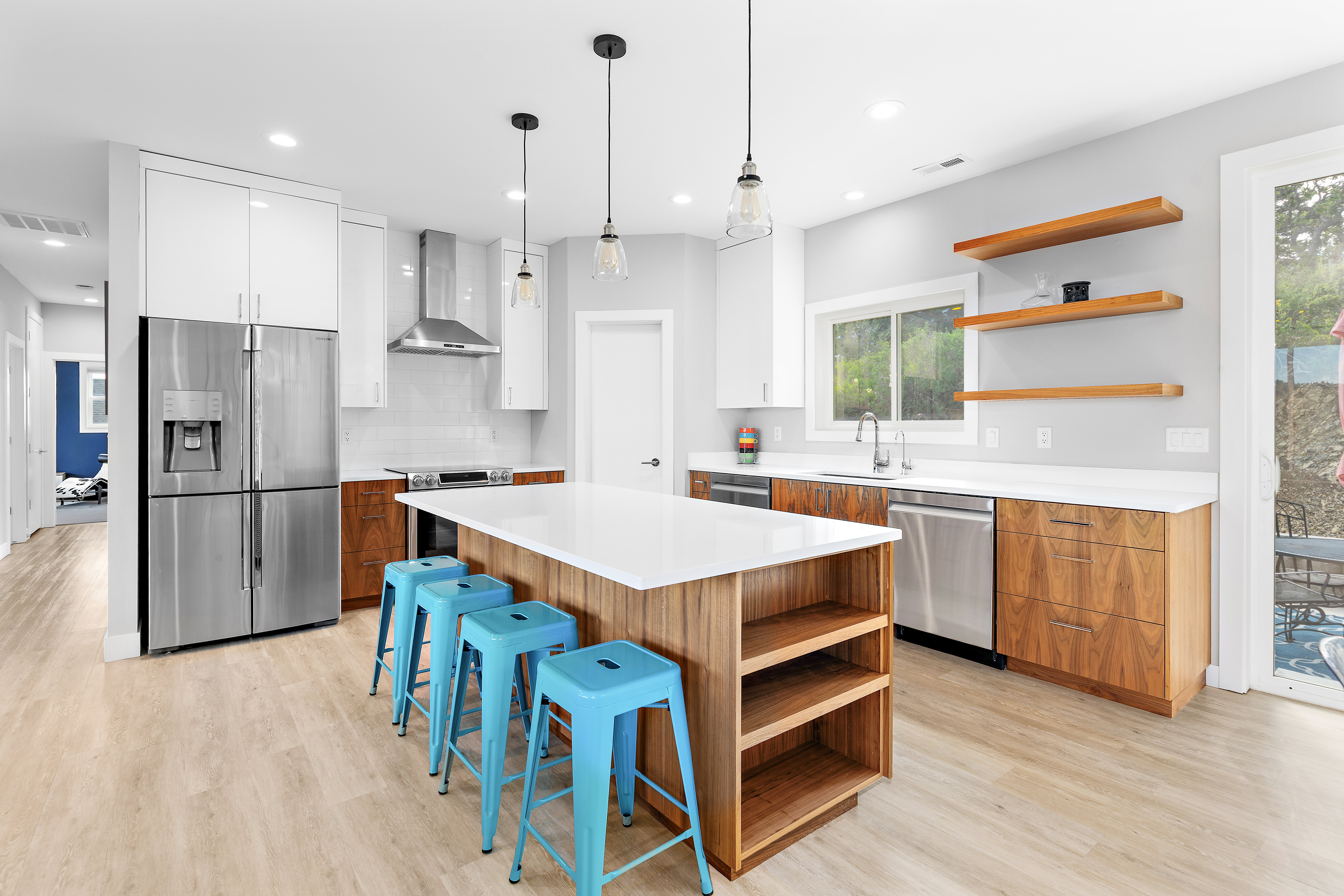 Open-concept kitchen featuring a large central island with a solid surface countertop, stainless steel appliances, warm wood-finish lower cabinetry, white upper cabinetry, and light wood-finish flooring