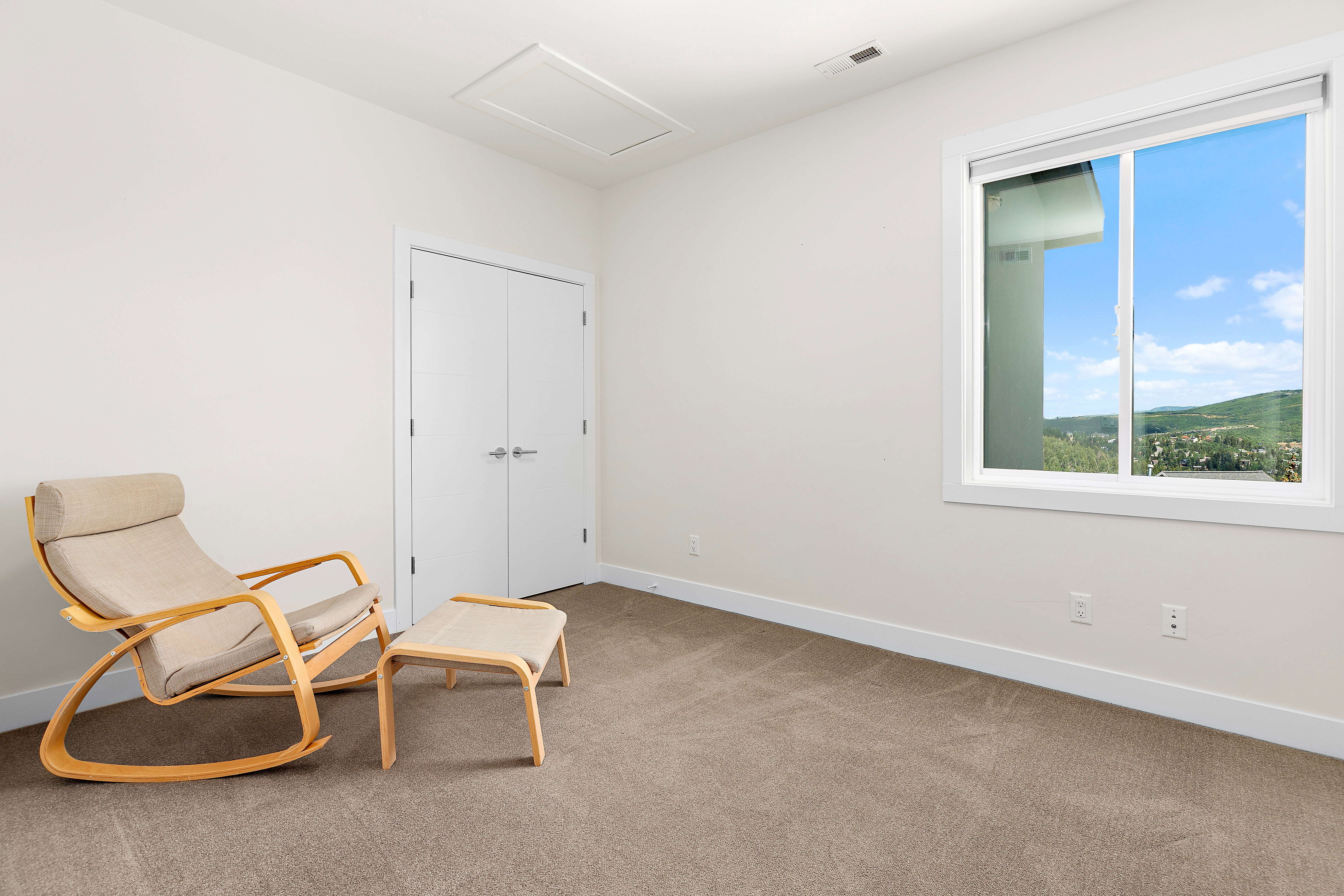 Light-filled interior space featuring a large window, neutral carpeting, and white walls