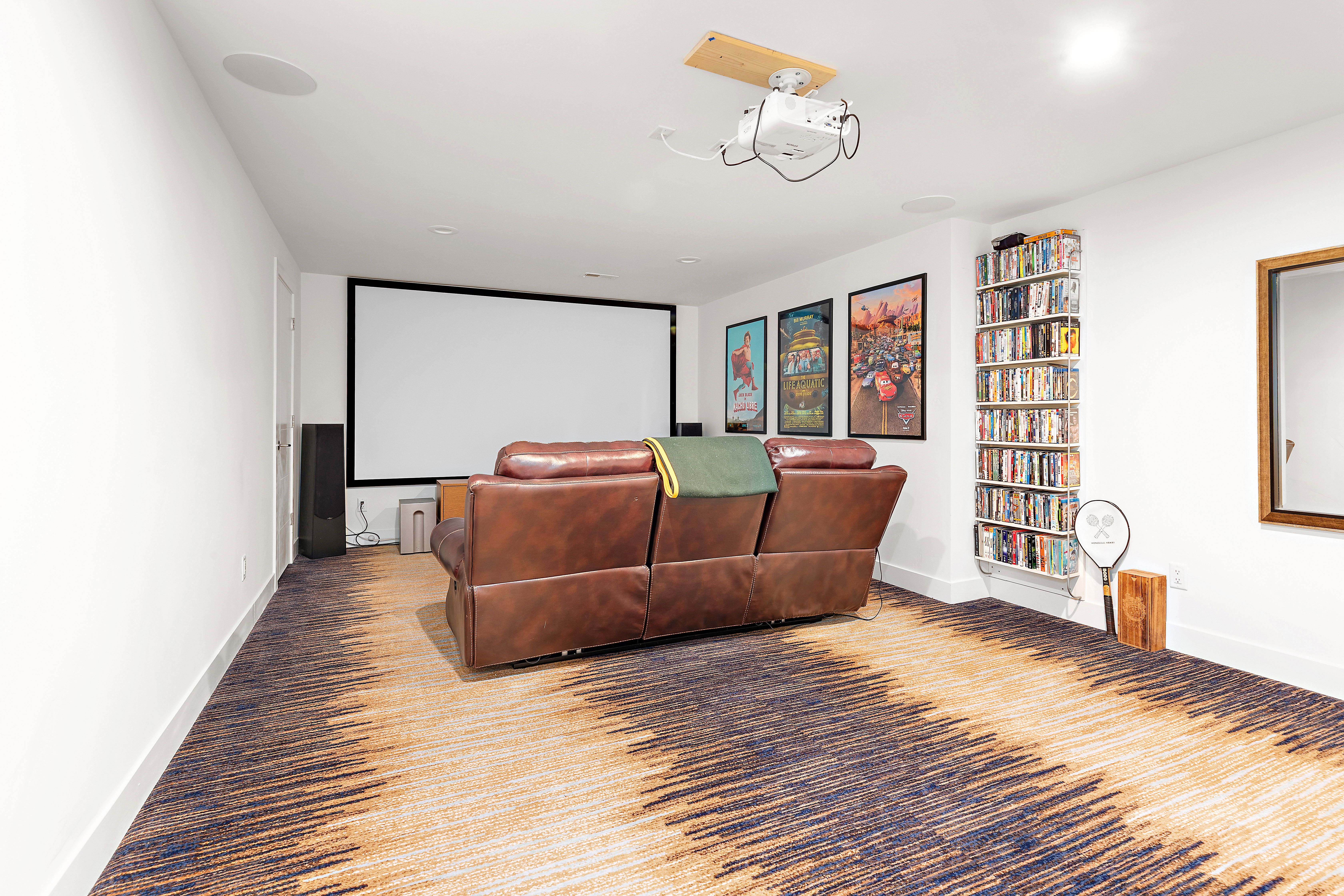 Dedicated media room featuring a large projector screen, ceiling-mounted projector, and integrated ceiling speakers