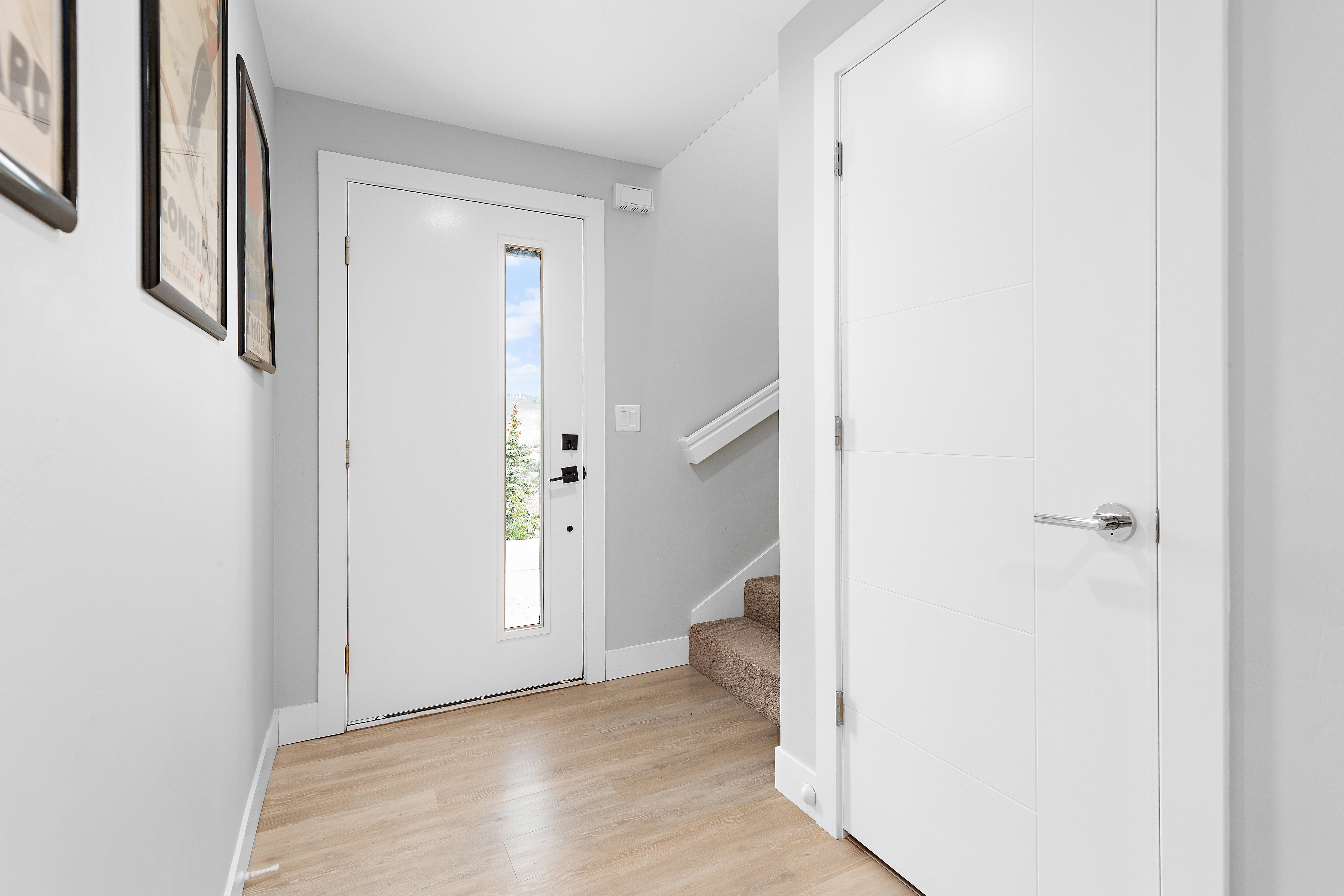 Bright entry featuring light wood-finish flooring, a contemporary white door with a vertical window pane, white baseboards, and light gray walls
