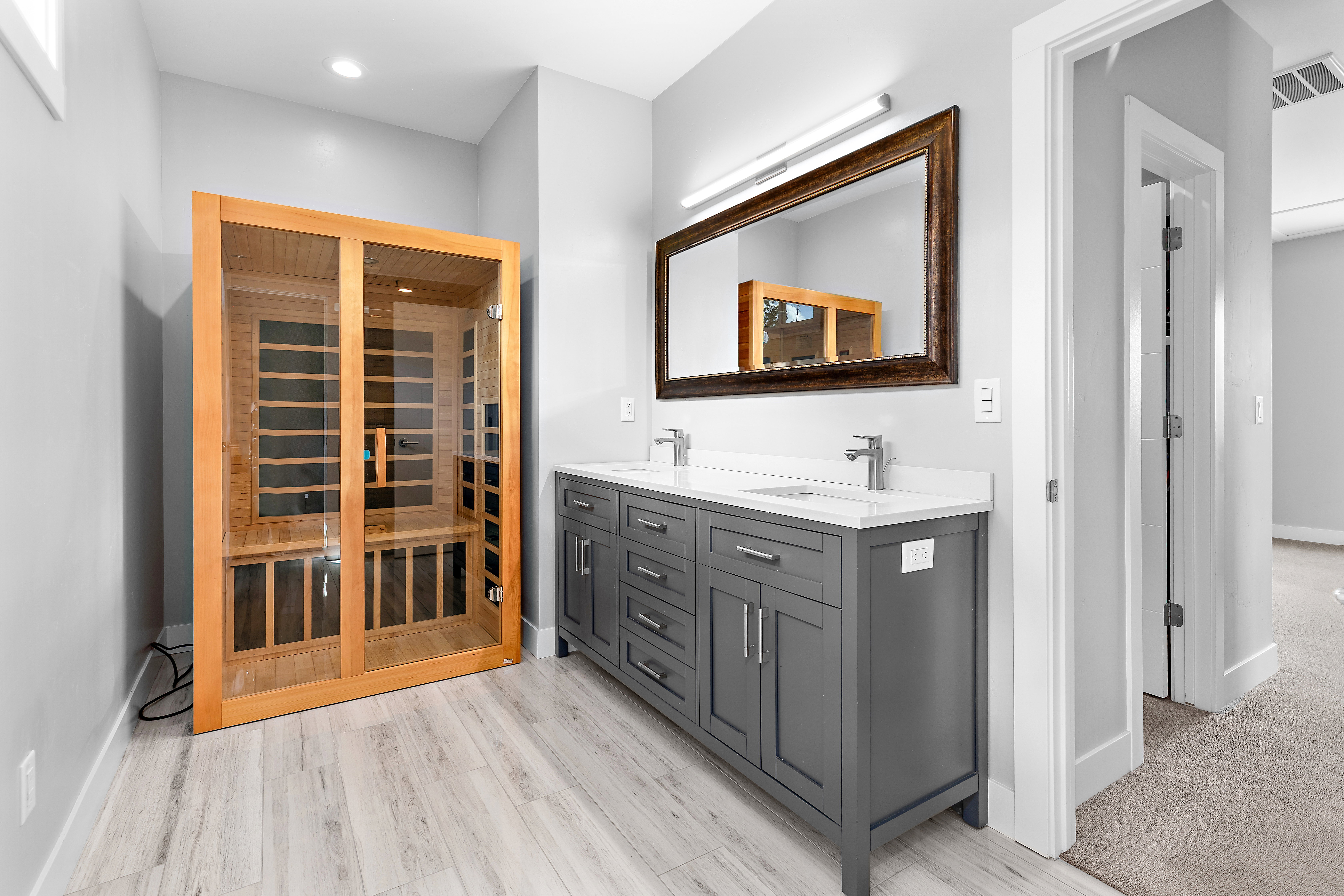 Freestanding sauna unit with a dual-sink vanity featuring gray cabinetry and a white countertop