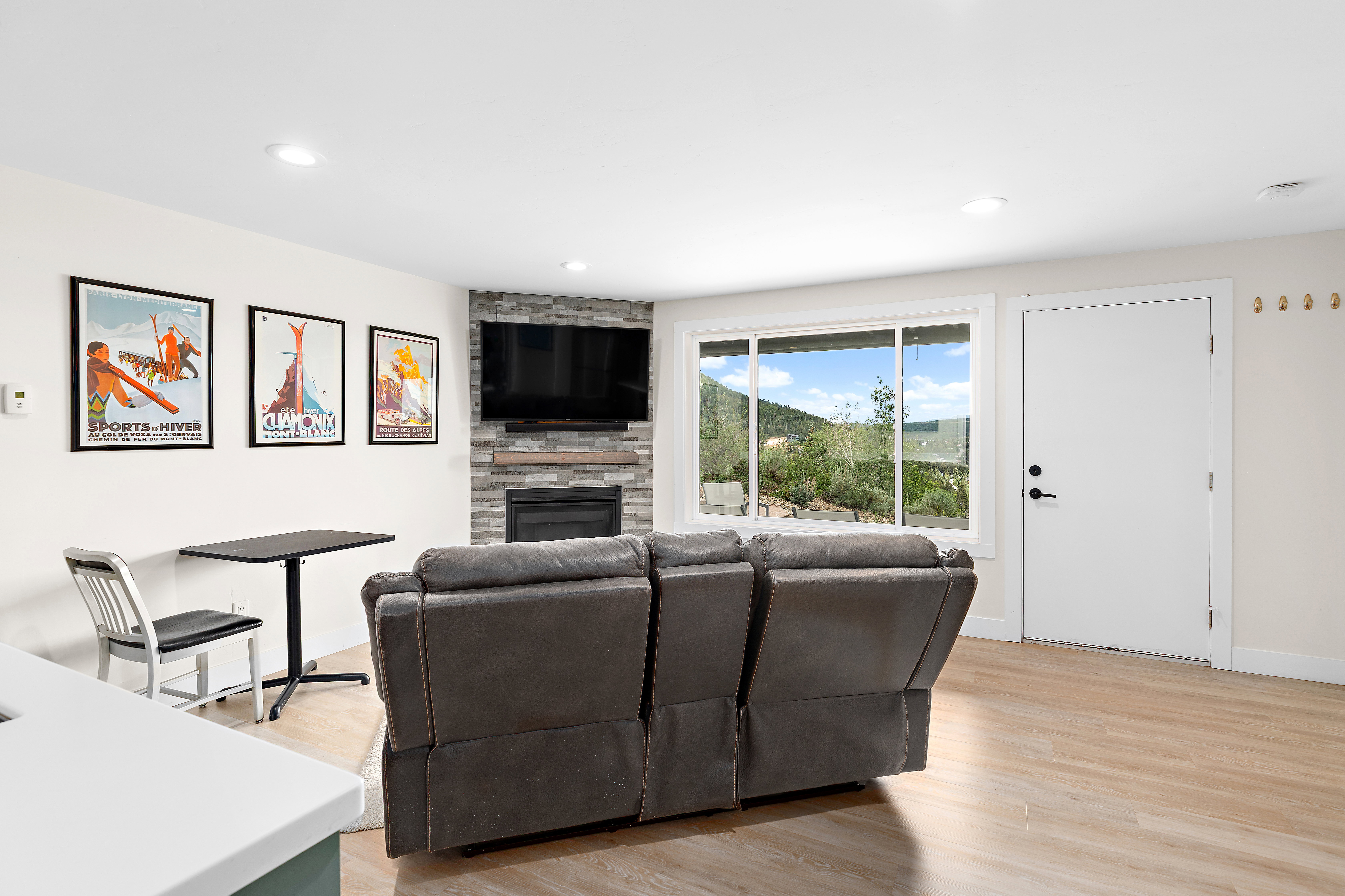 Living area featuring wood-finish flooring, a stone-clad fireplace with a built-in mantle, recessed lighting, and large windows