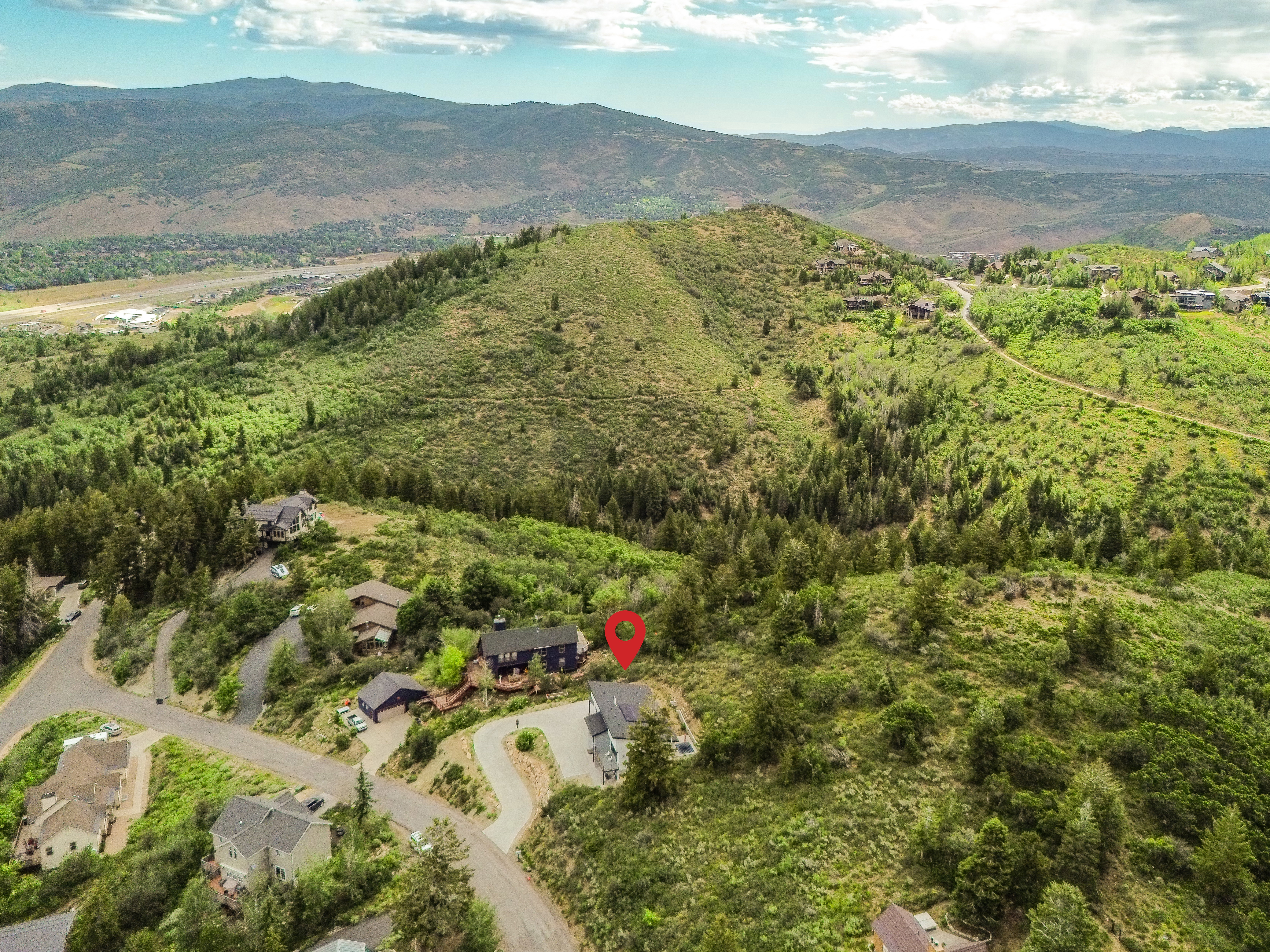 Aerial perspective showcasing a residential property nestled on a verdant hillside with winding paved roads