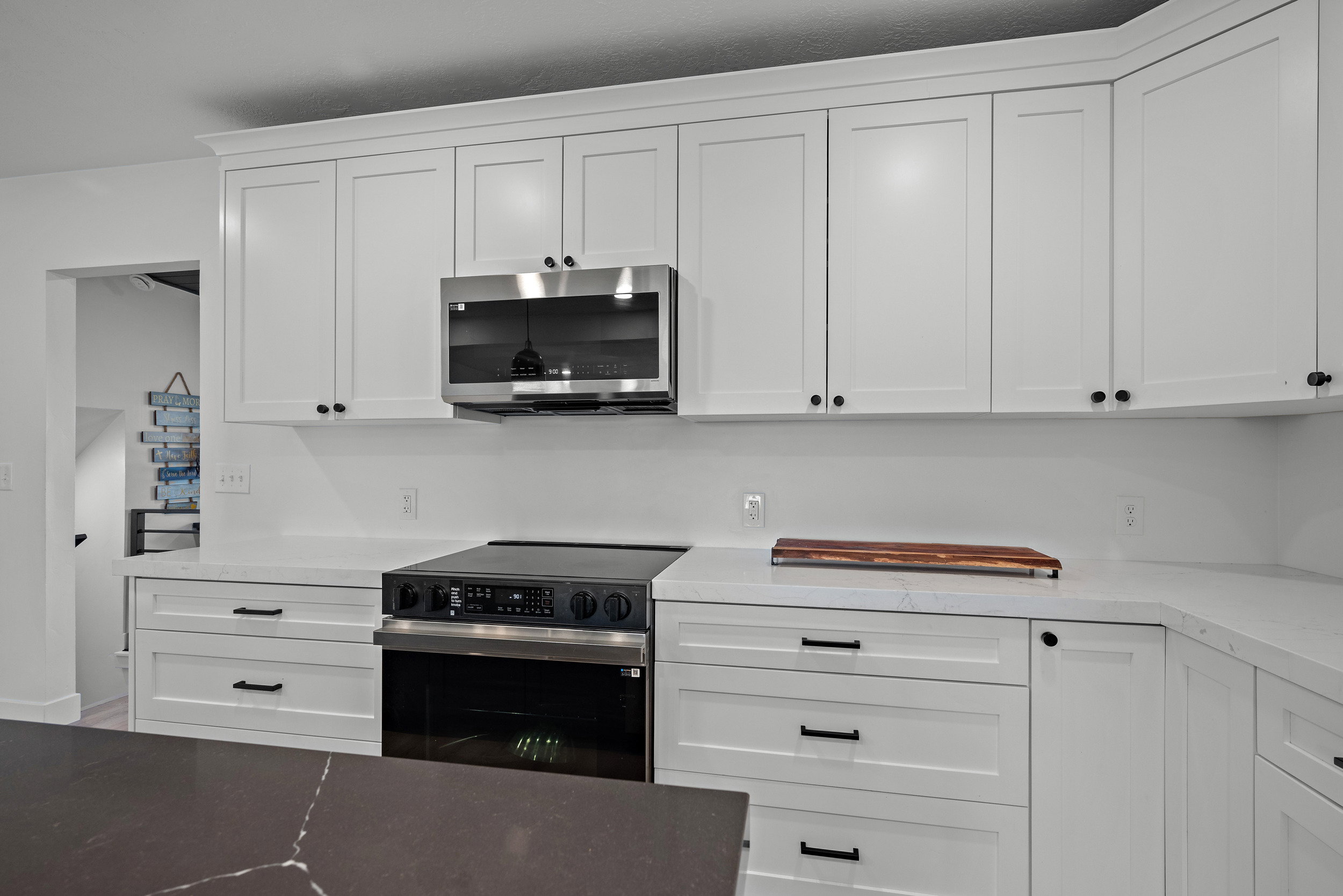 Modern kitchen featuring white shaker cabinetry, stainless steel microwave, black electric range, light countertops, and a dark island countertop