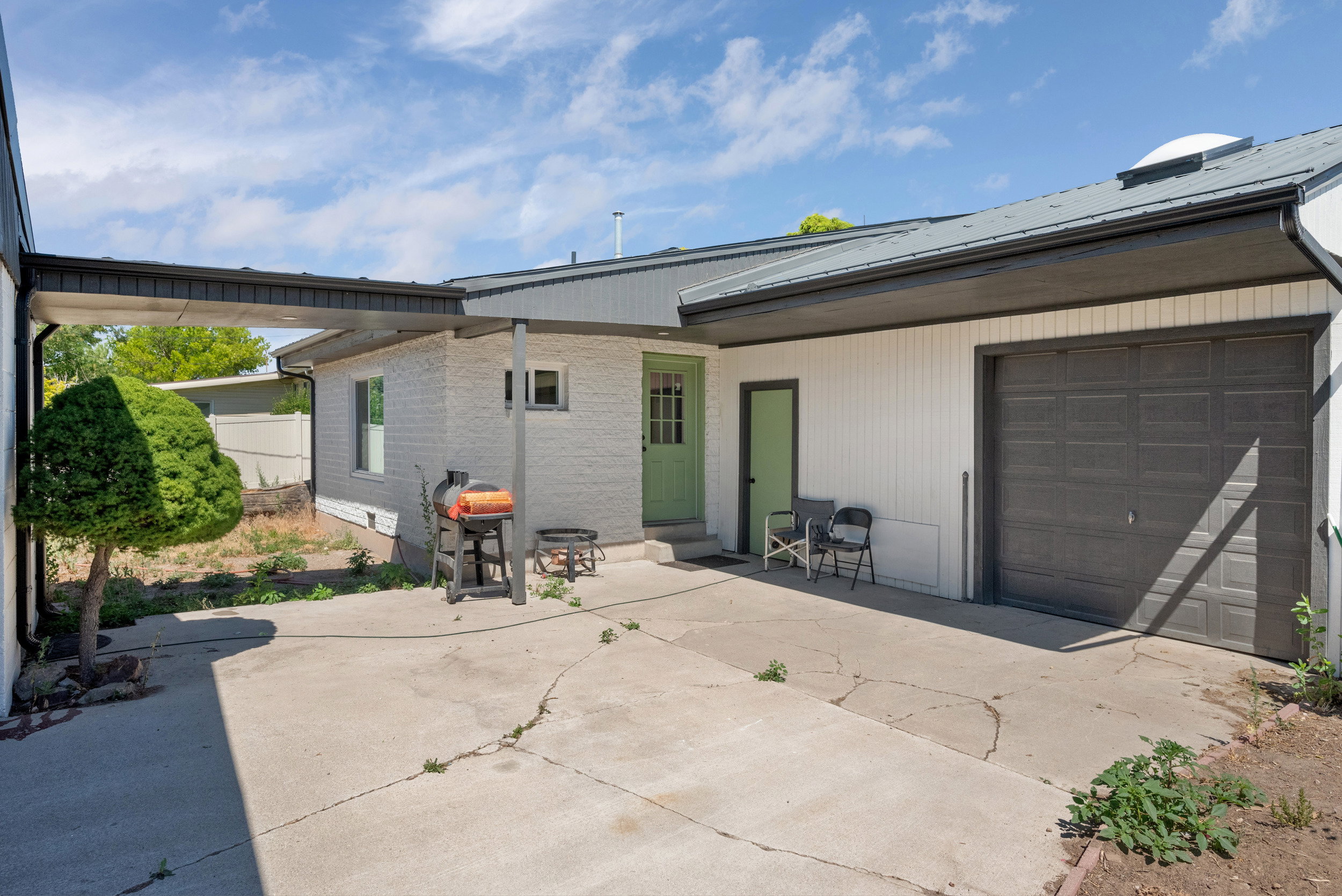Exterior featuring a covered walkway, painted brick siding, a metal roof, and an attached garage with a dark gray door