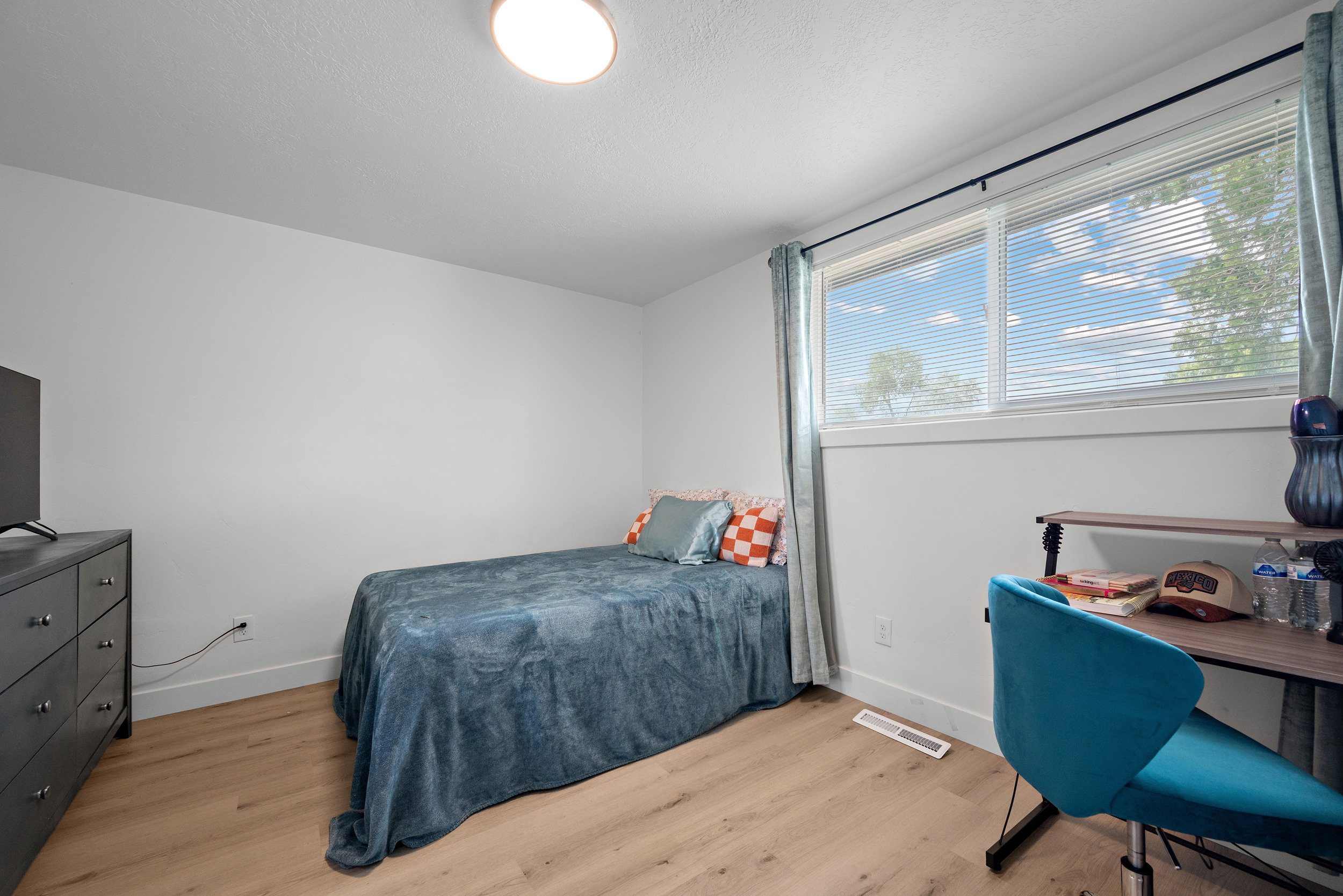 Bedroom featuring wood-finish flooring, a contemporary ceiling light fixture, and a large window with horizontal blinds