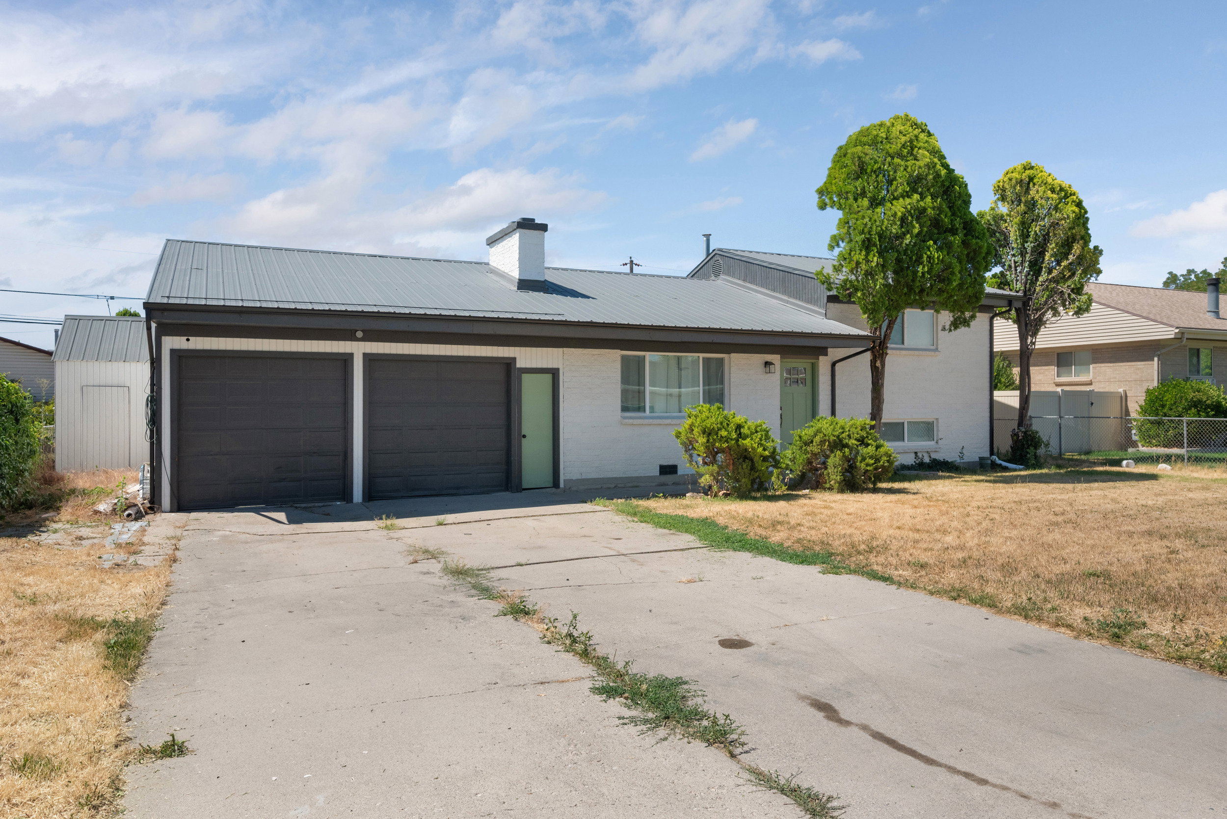 Single-story residence featuring a metal roof, attached two-car garage with dark doors, and a concrete driveway