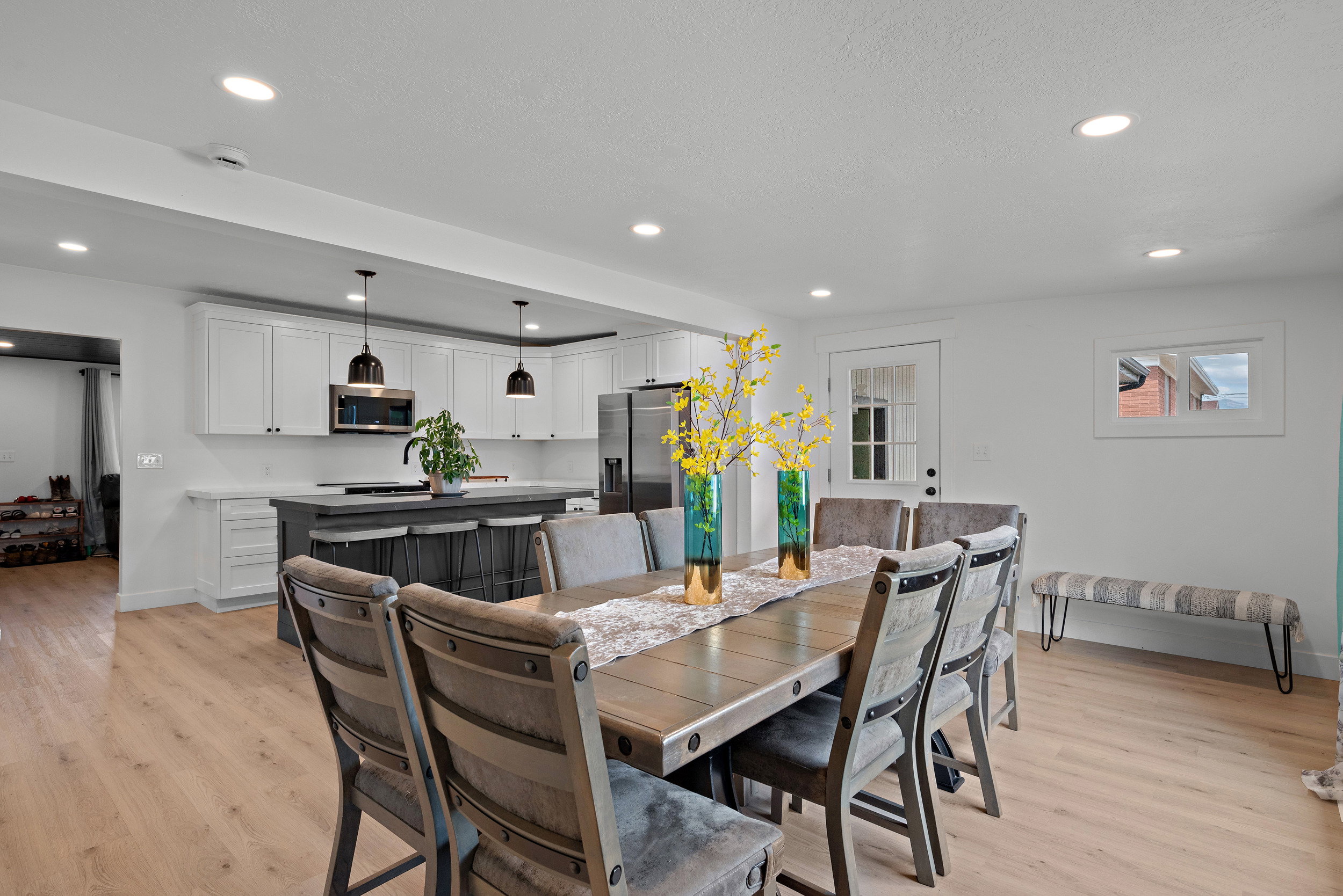Open-concept dining area with wood-finish flooring, recessed lighting, and a white paneled door with glass inserts