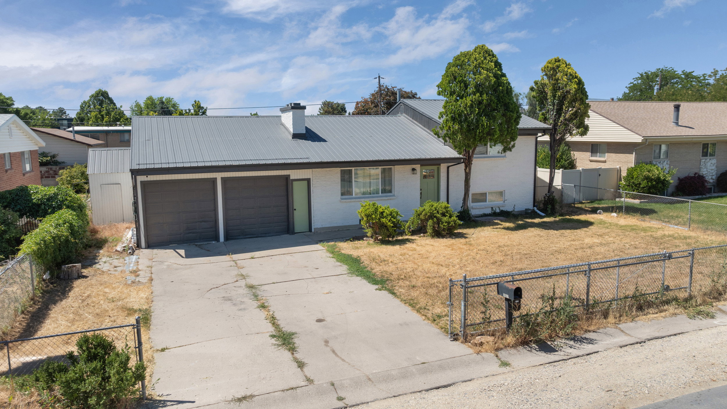 Ranch-style residence featuring a metal roof, attached two-car garage, and a front yard with mature trees
