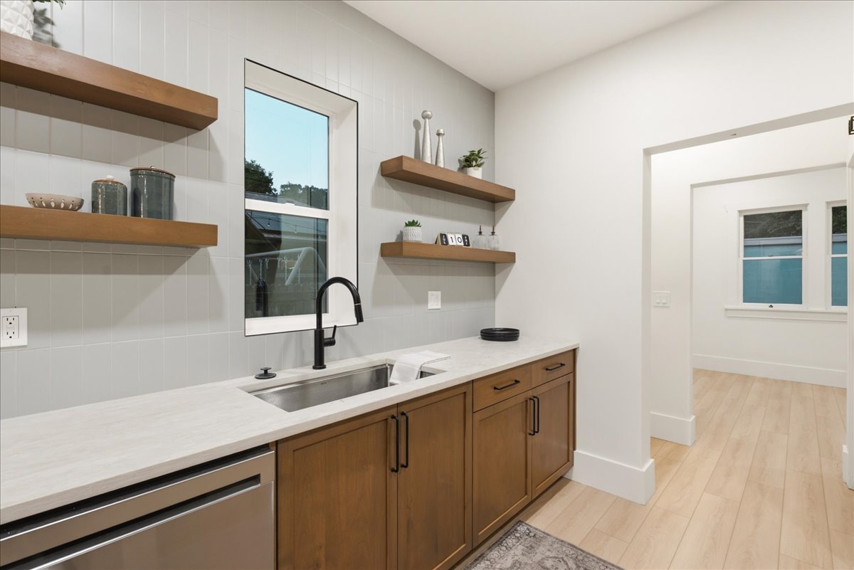 Kitchenette featuring a stainless steel undermount sink with a matte black faucet, light-toned countertops, and wood-finish cabinetry with black hardware