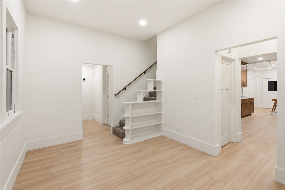 Open living area featuring light wood-finish flooring, recessed lighting, and a staircase with integrated shelving
