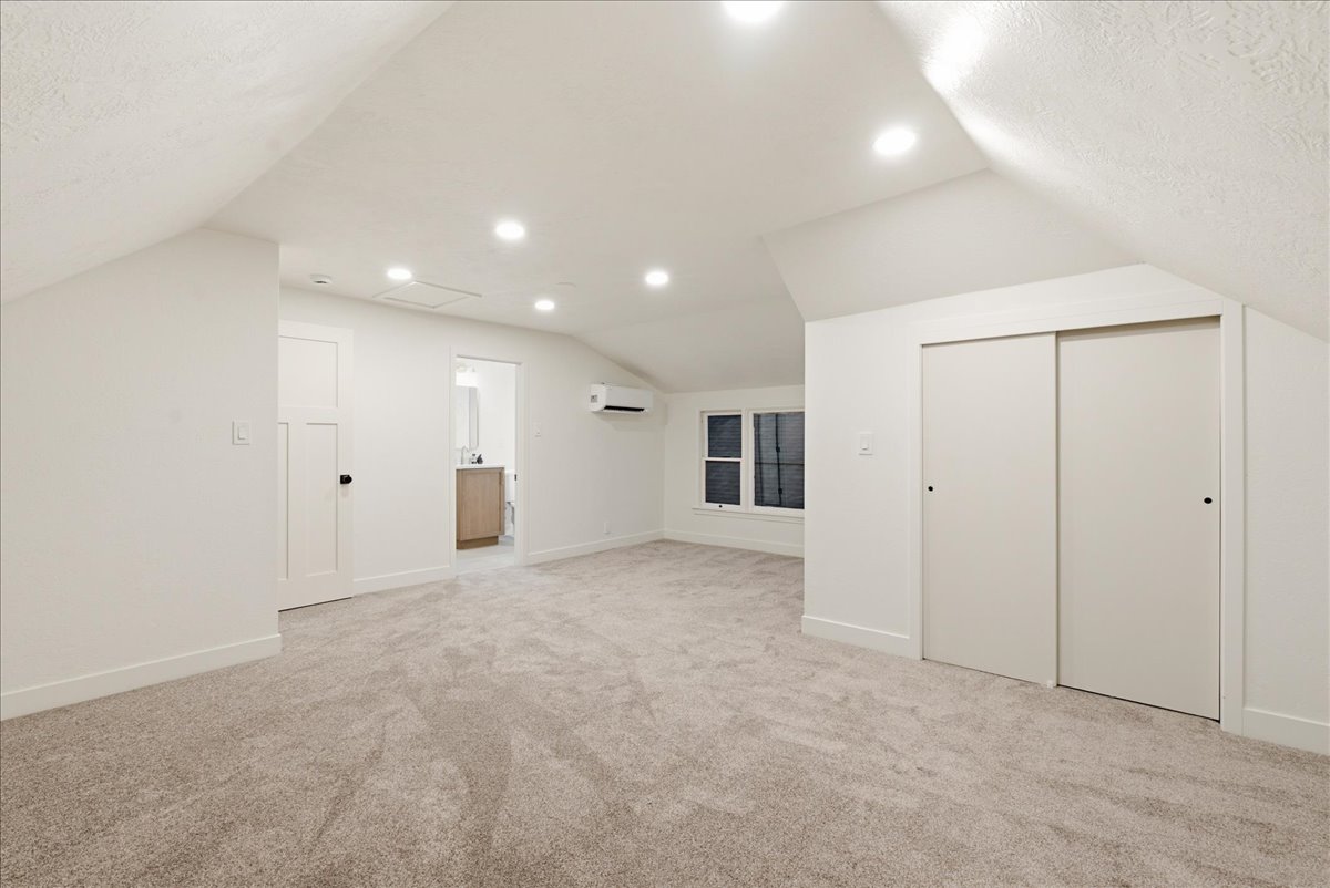 Spacious room featuring vaulted ceilings, recessed lighting, neutral-toned carpeting, white trim work, and a built-in split-system air conditioning unit
