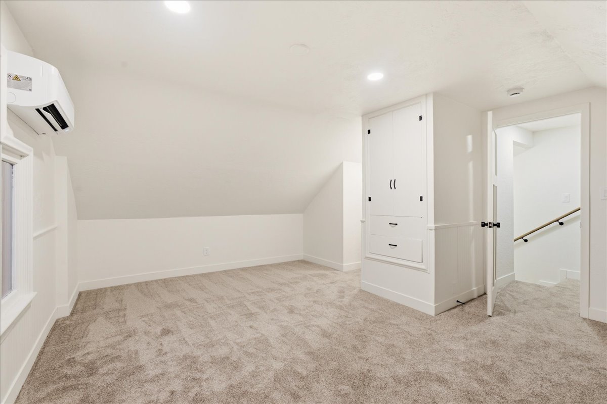 Carpeted room featuring a built-in cabinet with two doors and two drawers, a window, a wall-mounted AC unit, and recessed lighting