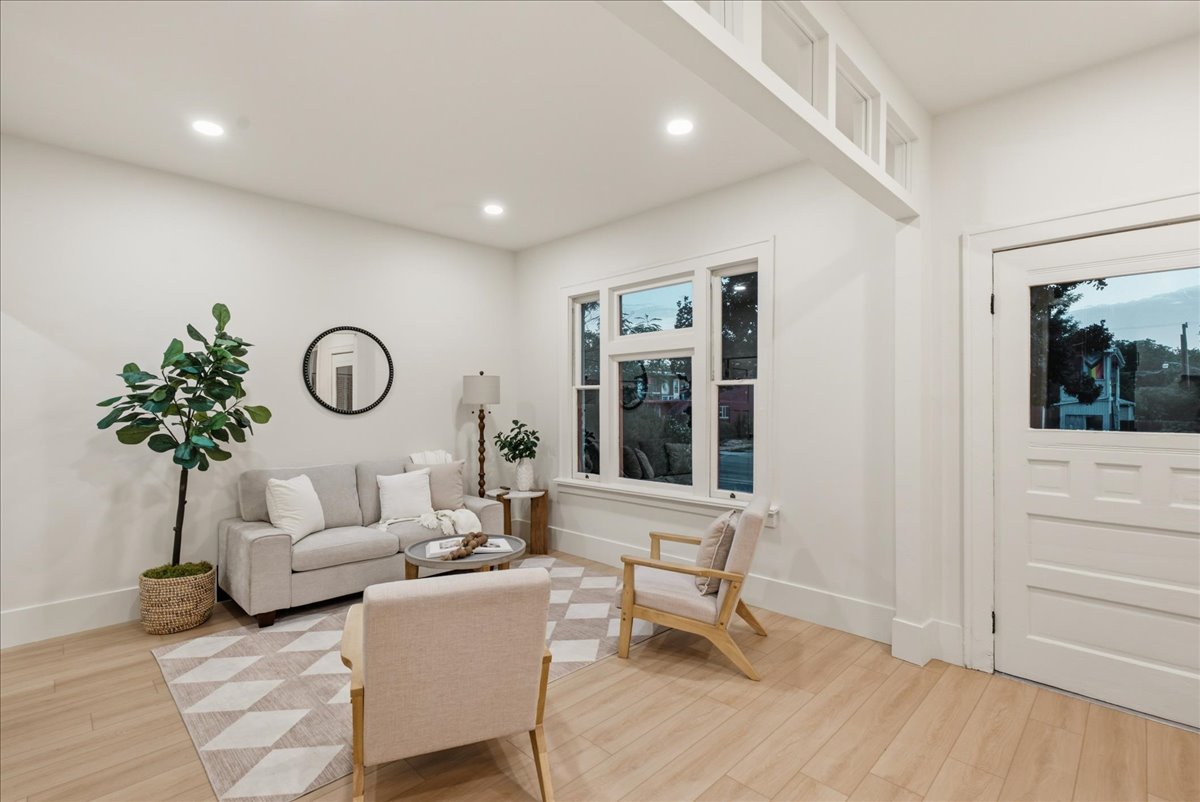 Spacious living area featuring light wood-finish flooring, white walls, recessed lighting, and a large multi-pane window