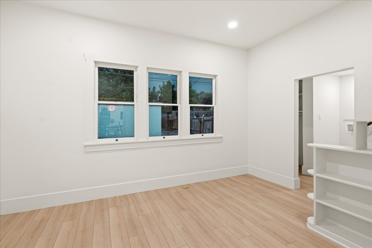 Room featuring wood-finish flooring, three windows with white trim, recessed lighting, and an open doorway