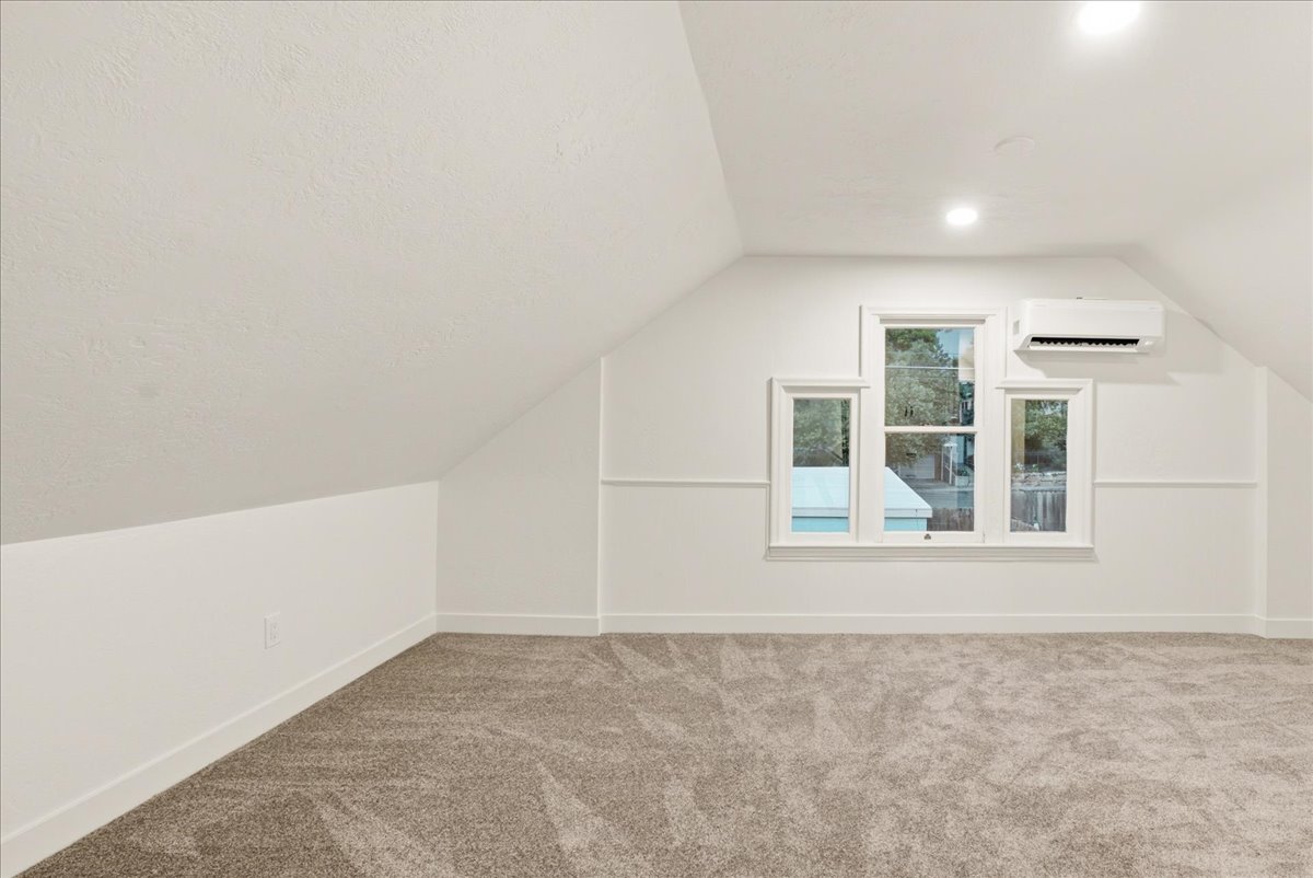 Spacious room featuring sloped ceilings, plush carpet flooring, and white trim