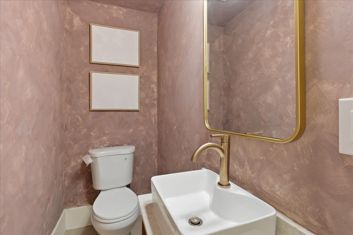 Powder room featuring textured pink walls, a rectangular vessel sink, a gold-framed mirror, and a gold-finish faucet