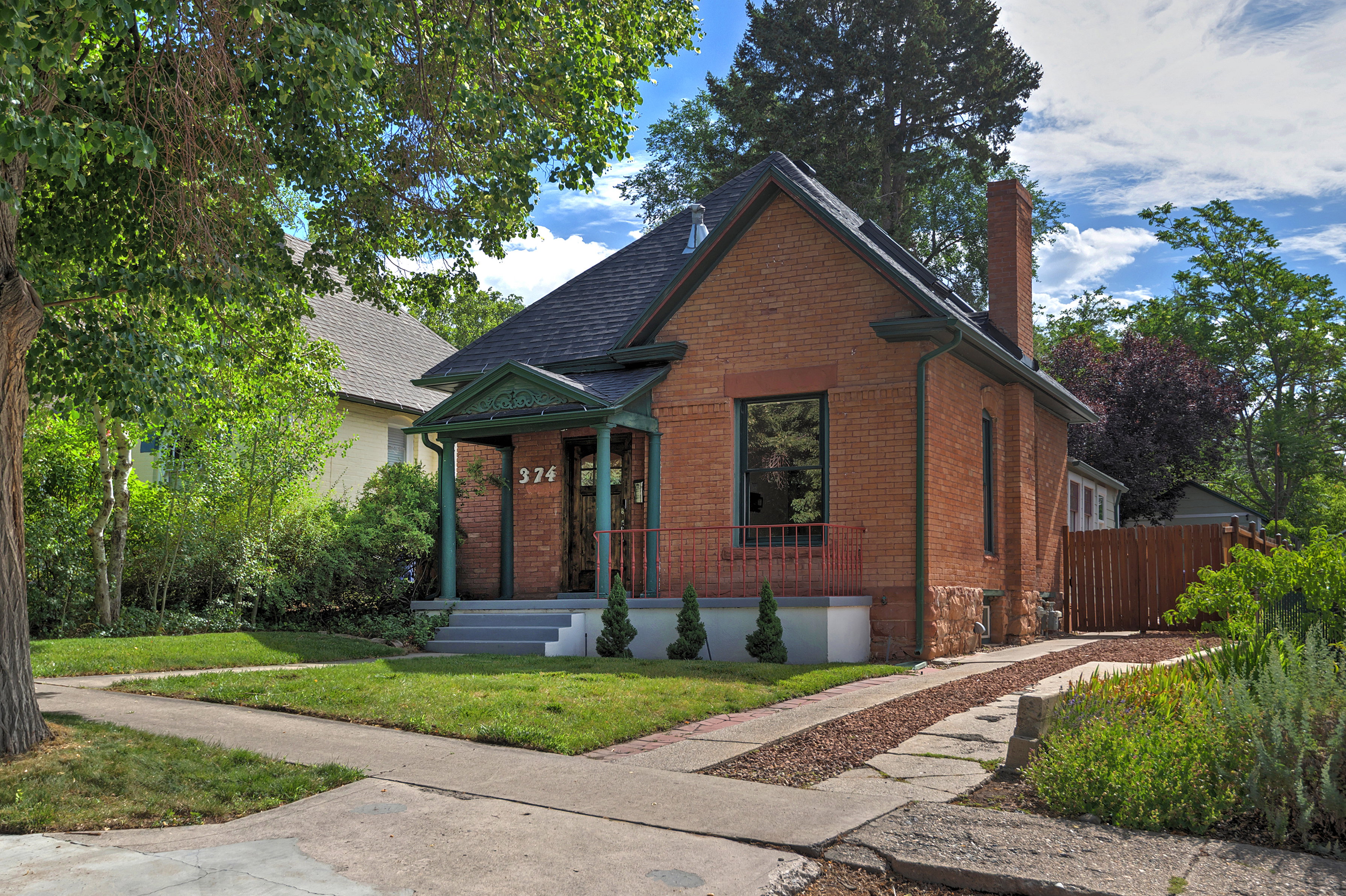 Brick exterior featuring a covered front porch with decorative trim, a stone foundation accent, and a prominent chimney