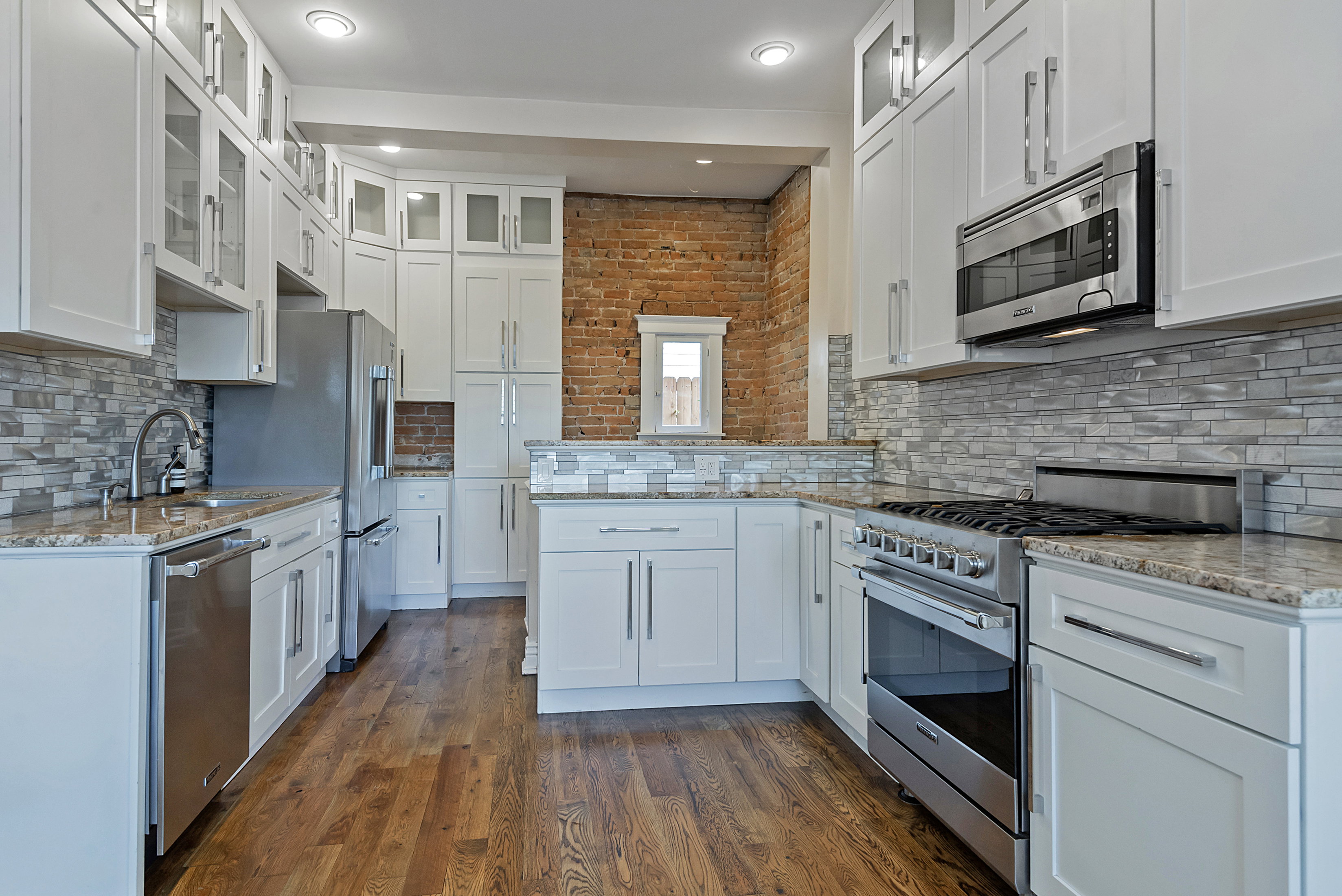 Modern kitchen featuring white shaker cabinetry, stainless steel appliances, granite countertops, and a stacked stone backsplash