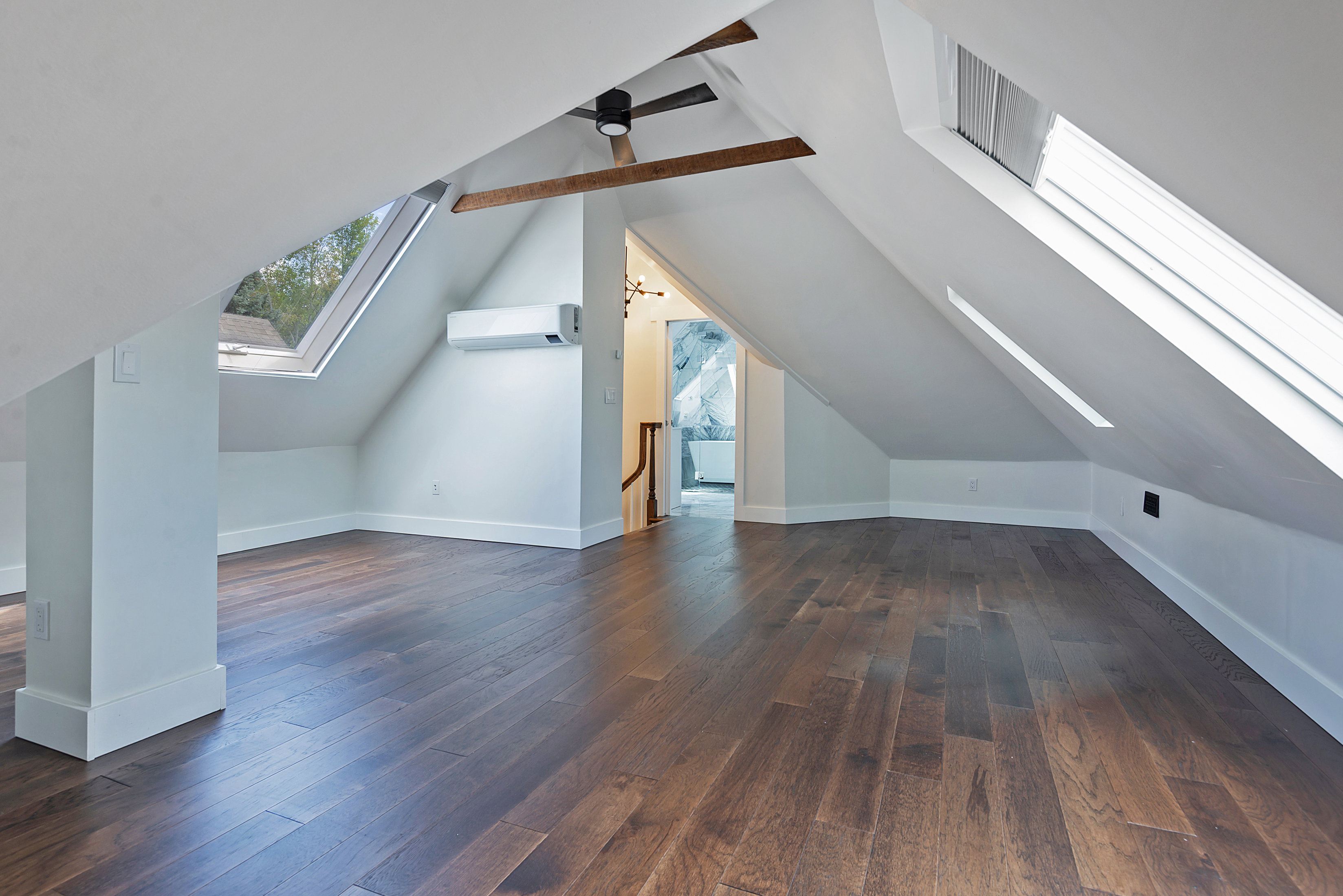 Attic space featuring wood-finish flooring, multiple skylight windows, exposed wood beams, and a ceiling-mounted fan