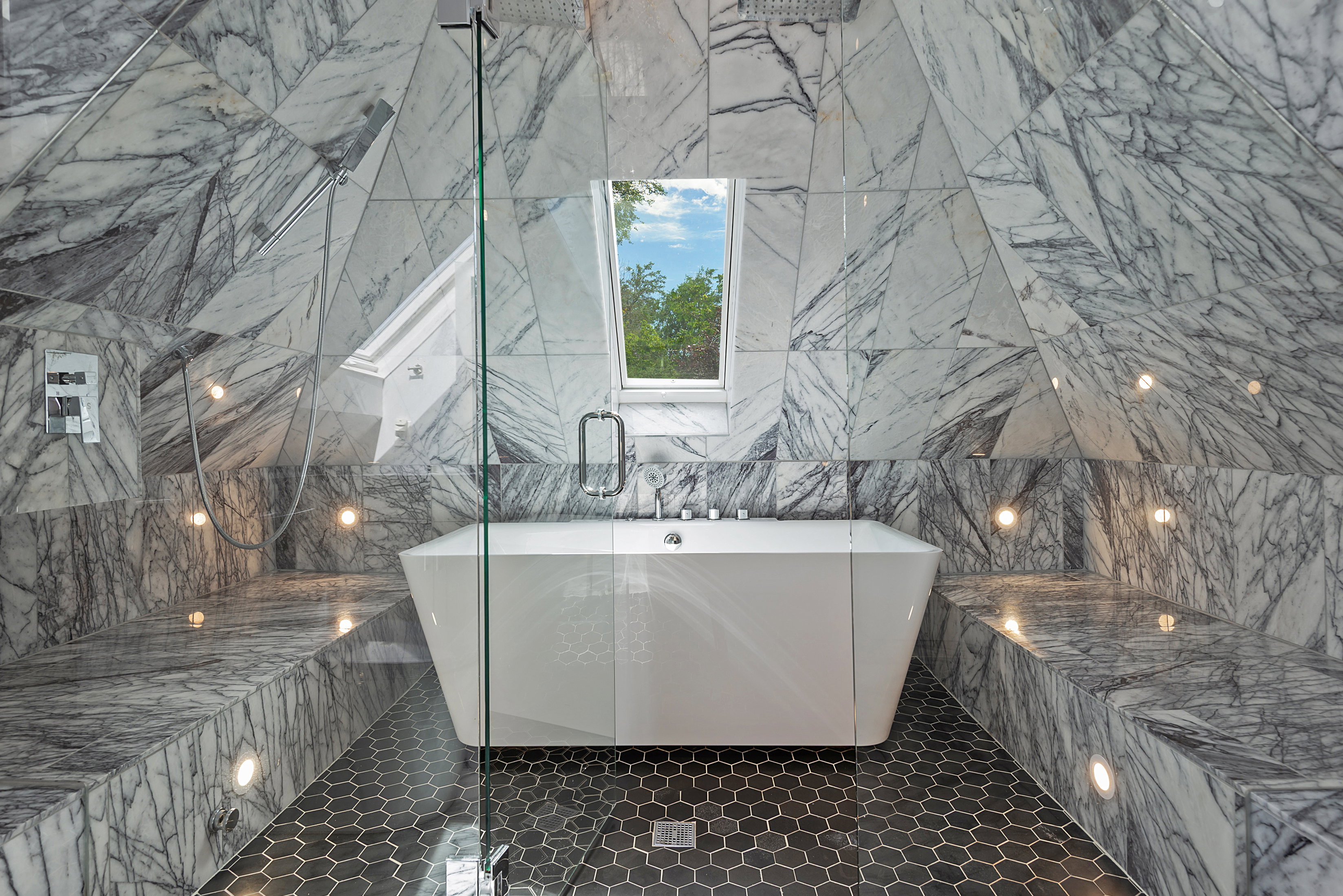 Freestanding soaking tub with a wall-mounted faucet, surrounded by geometric marble wall and bench seating