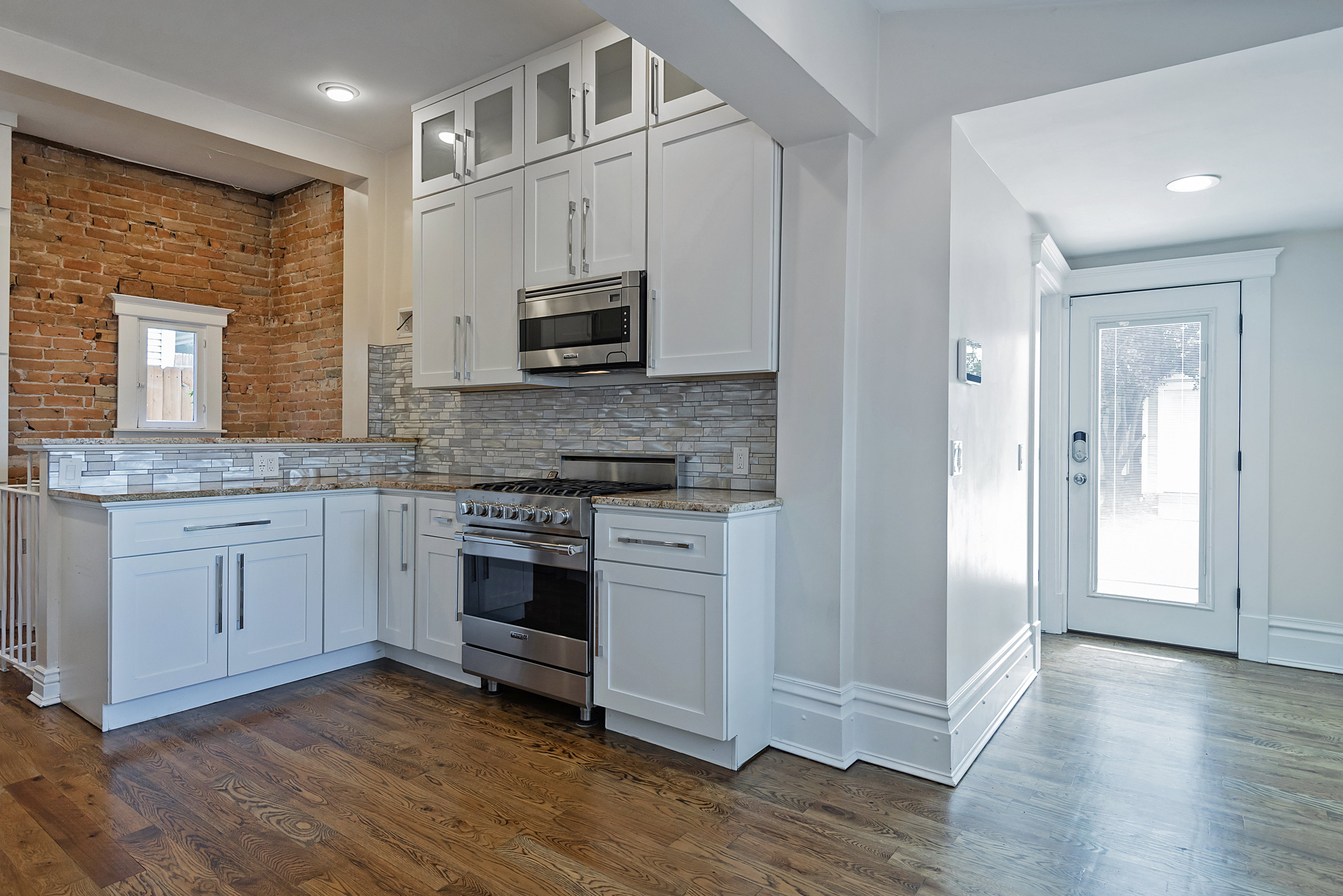 Contemporary kitchen featuring white cabinetry, stone countertops, a stainless steel gas range, microwave, and wood-finish flooring