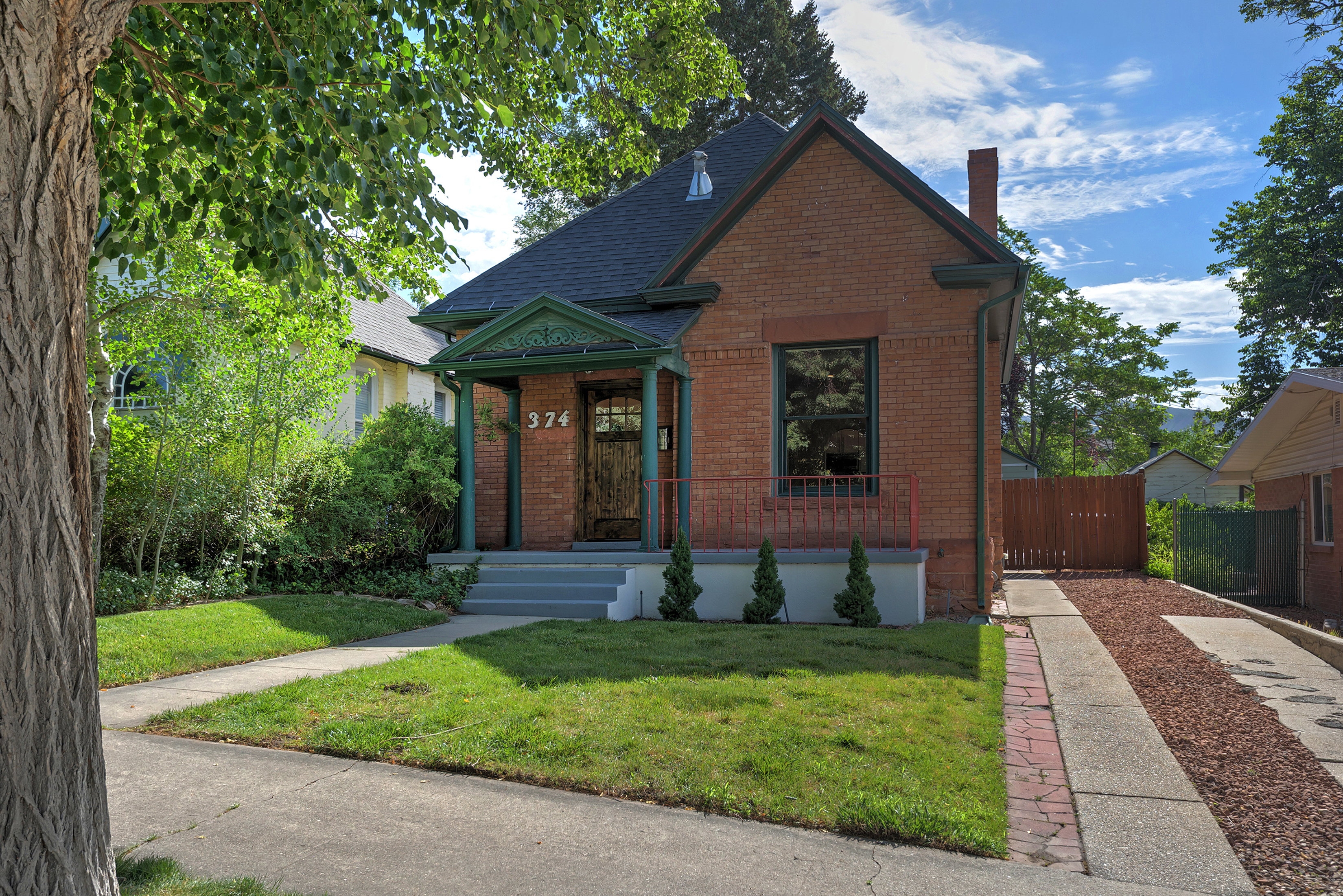 Brick-clad exterior featuring a covered front porch with decorative trim, a paved walkway, a gravel driveway, and mature landscaping
