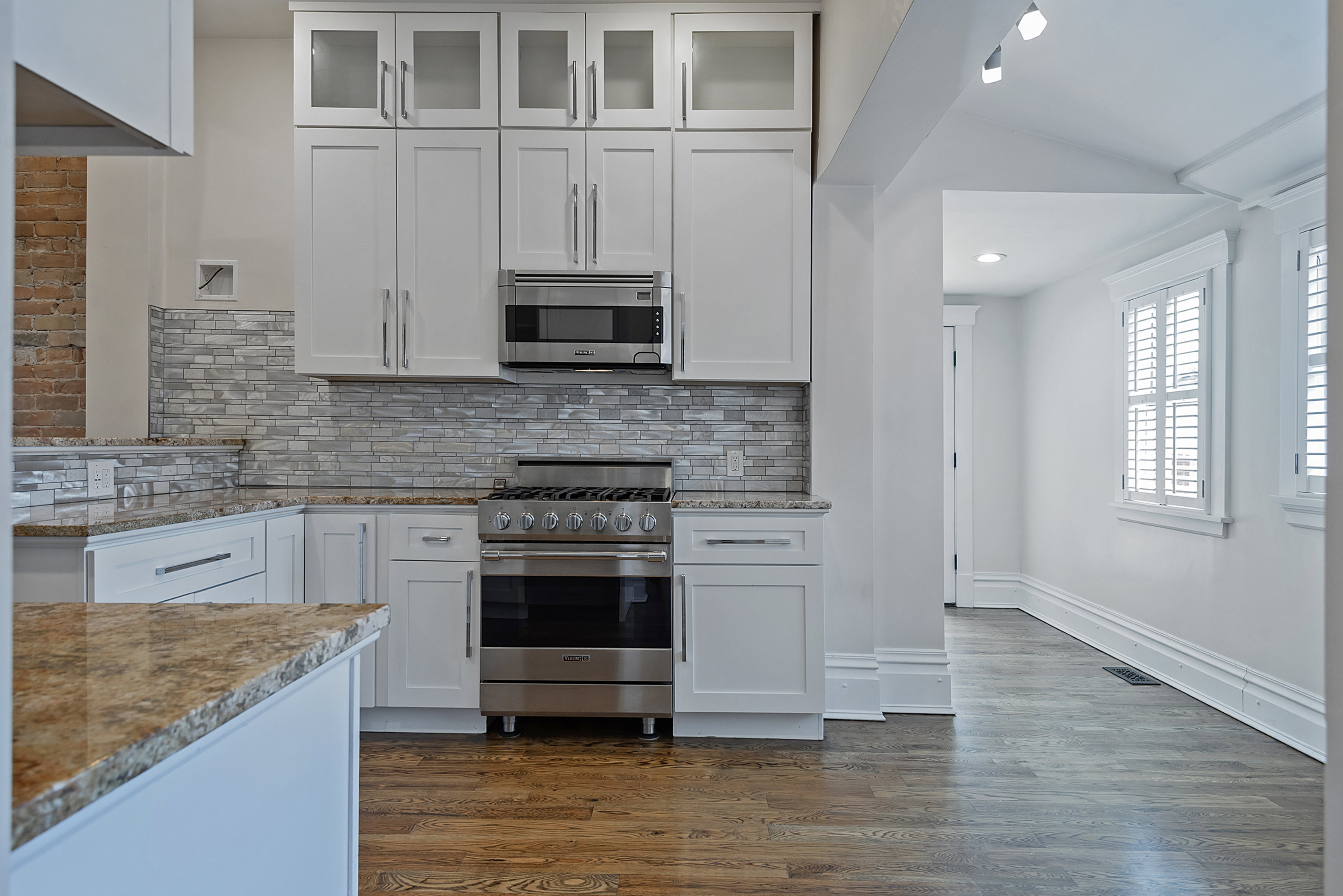 Modern kitchen featuring white cabinetry, stainless steel appliances, granite countertops, and a stacked stone backsplash