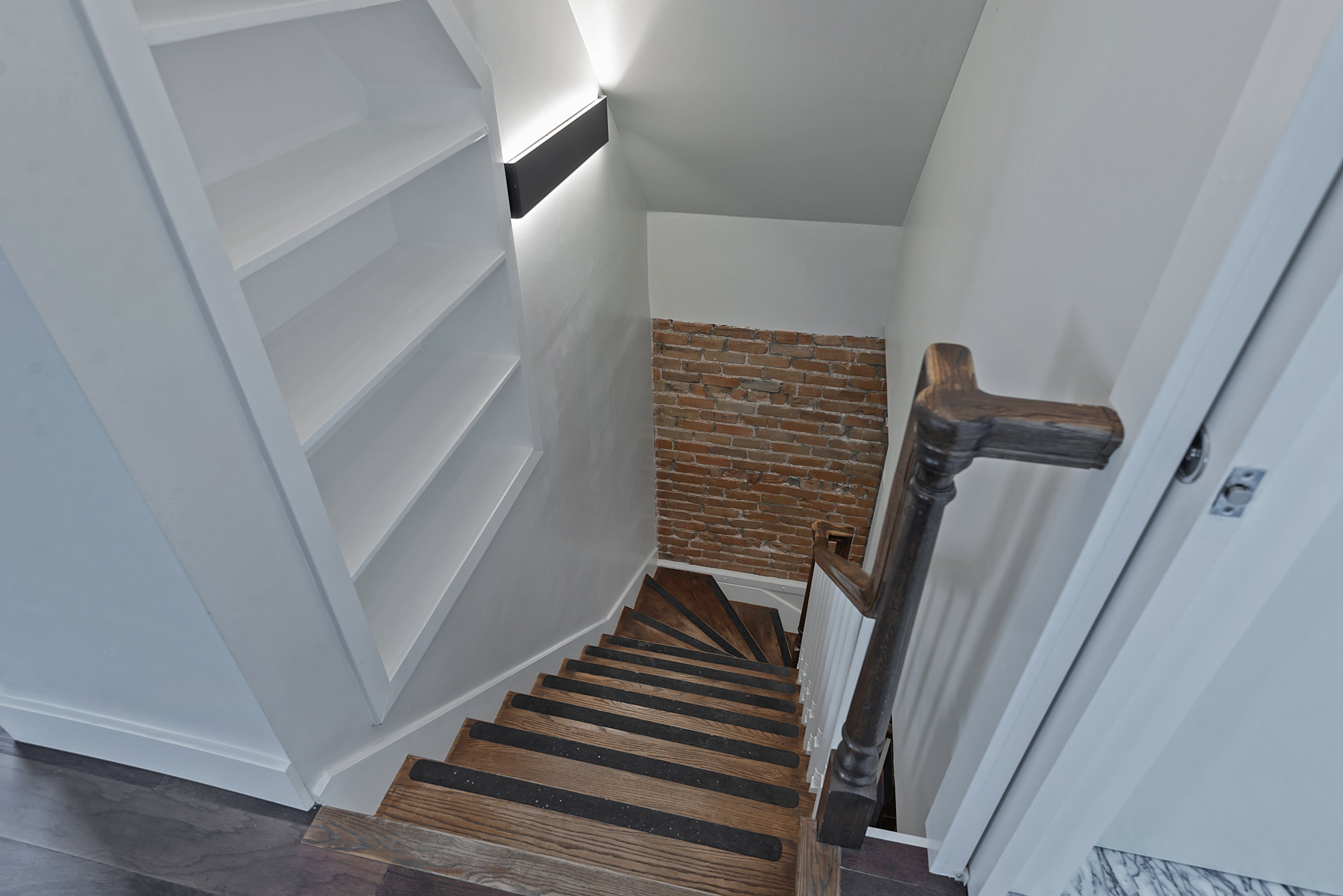 Hardwood staircase with dark wood railing and exposed brick accent wall