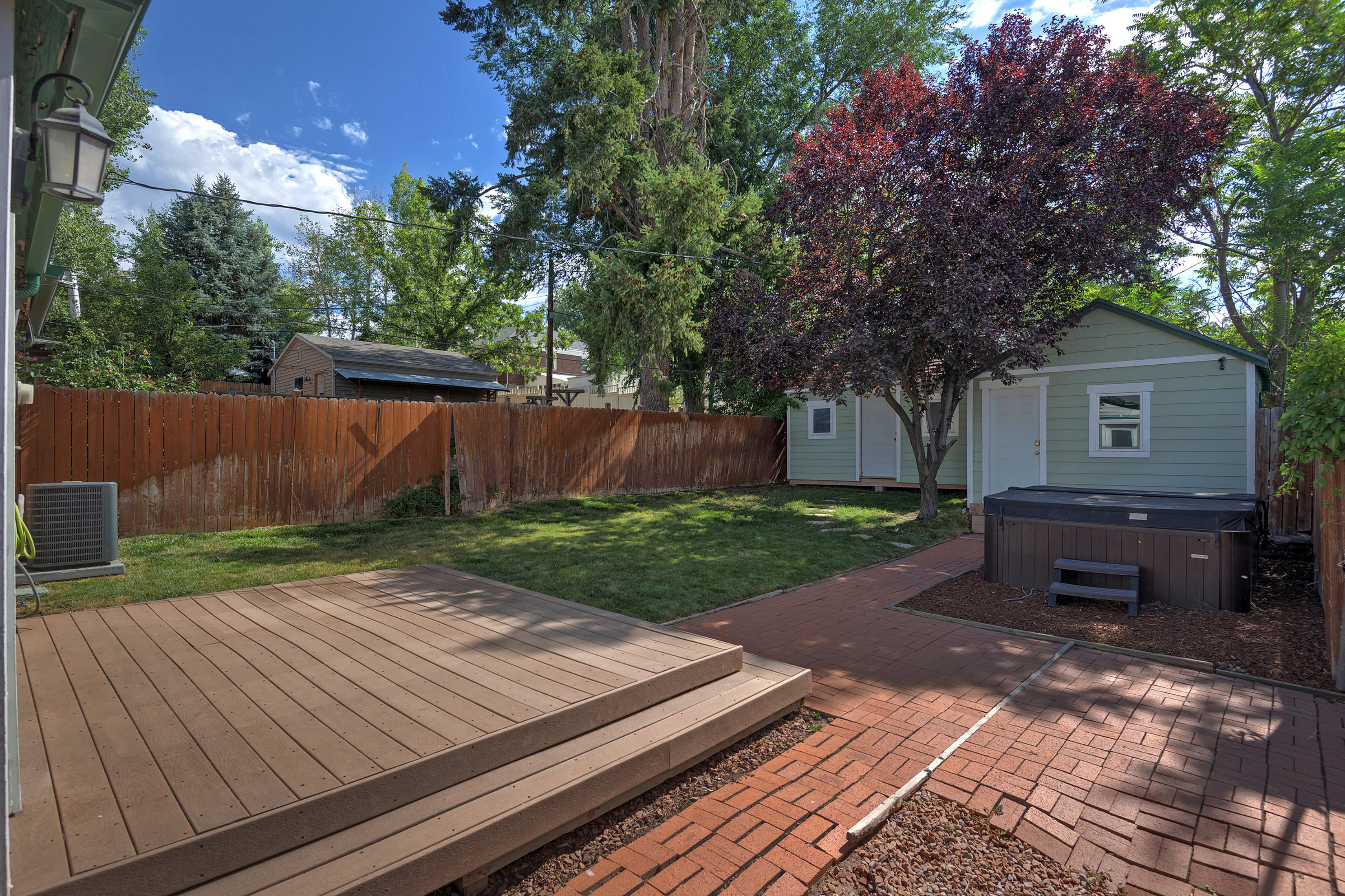 Expansive backyard featuring a composite deck, brick paver patio, lush lawn, and a privacy fence