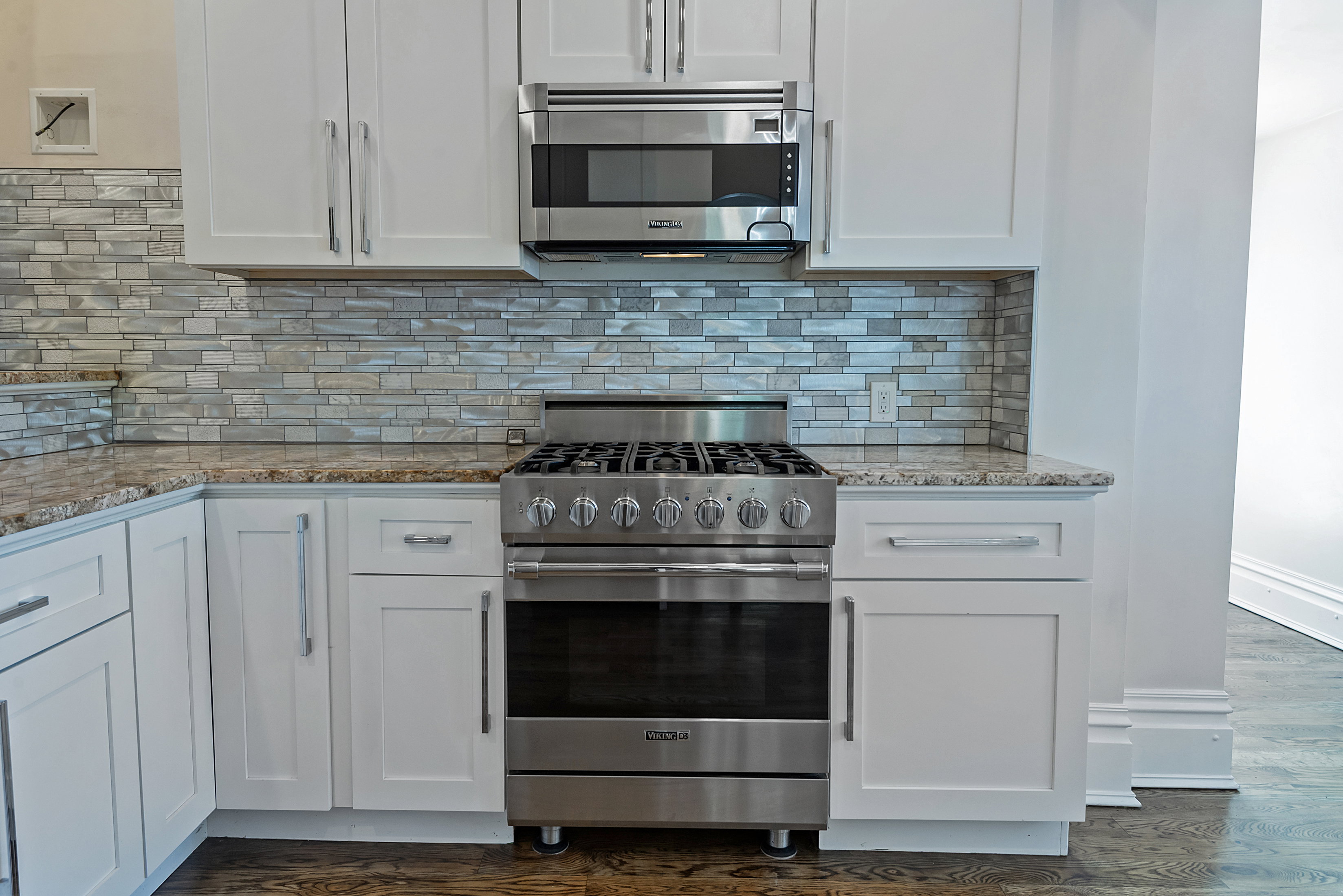 Gourmet kitchen featuring a stainless steel range and microwave, white shaker cabinetry, stone countertops, and a textured tile backsplash